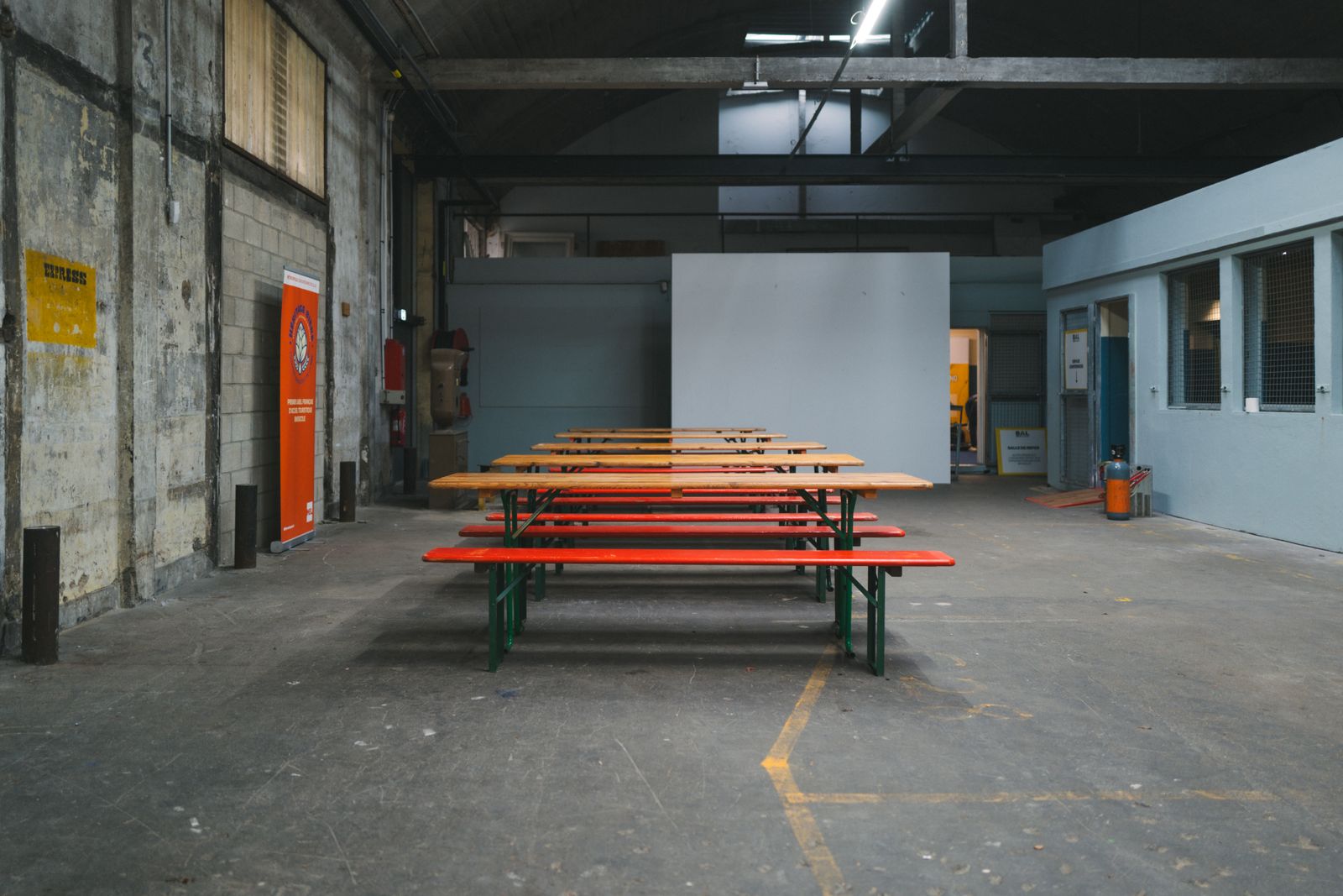 Long wooden tables and benches in an empty industrial hall with a concrete floor
