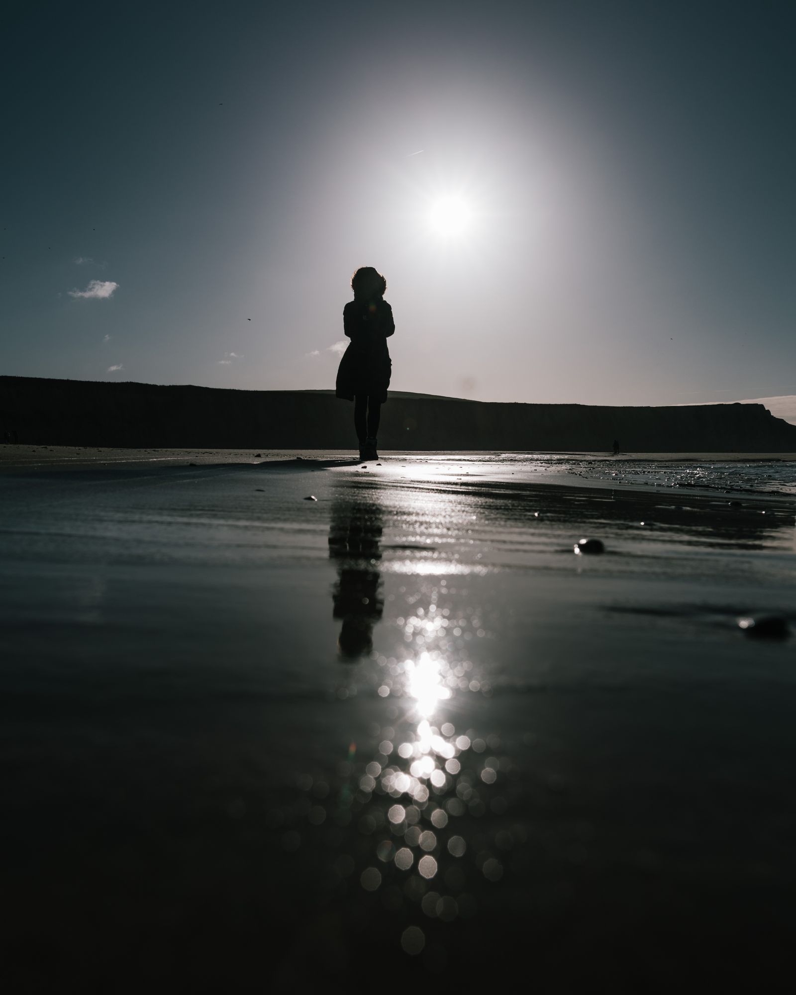 A person walking along the shore at sunset, reflected in the wet sand