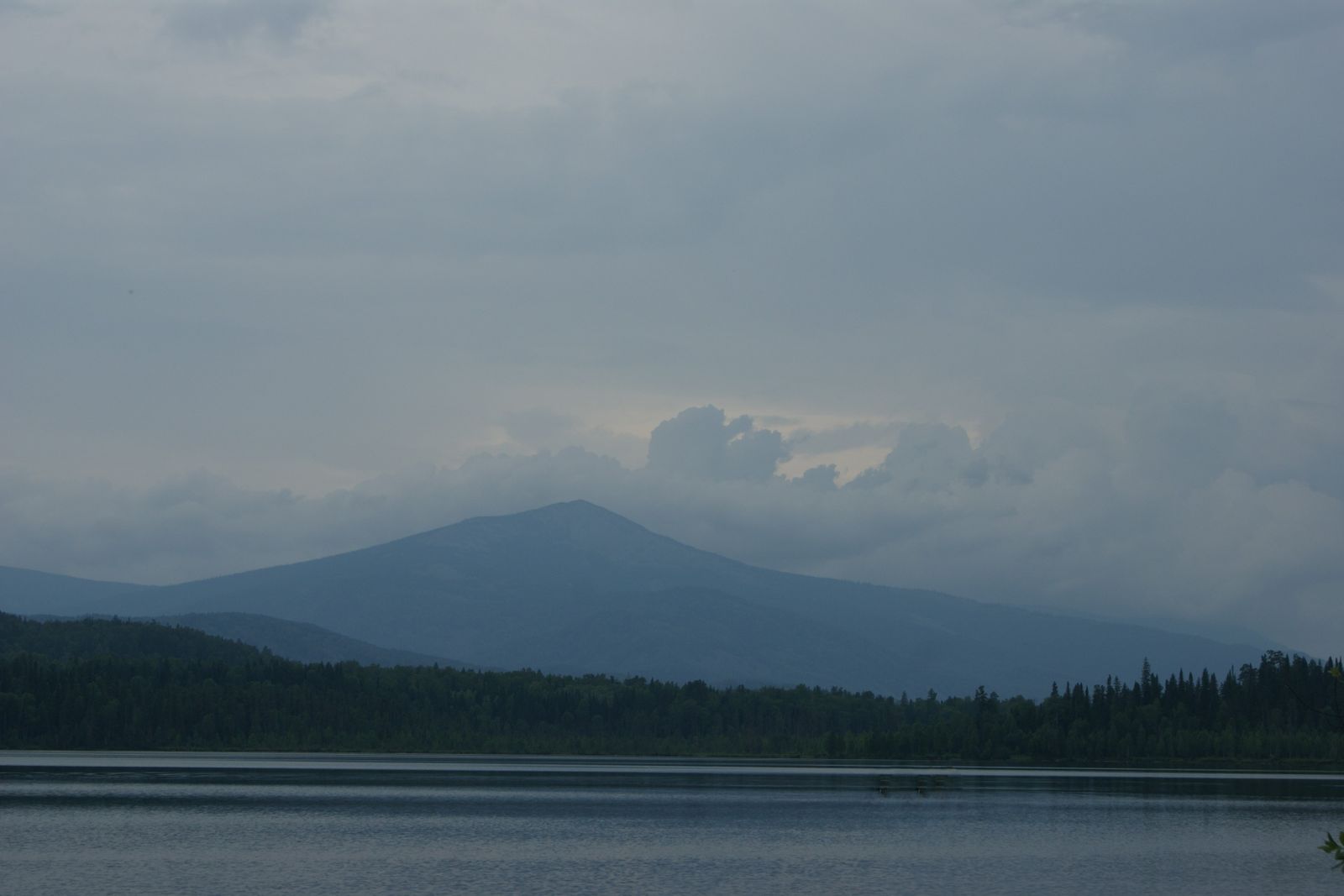 A mountain lake under a low grey sky, with dark forest on the far shore