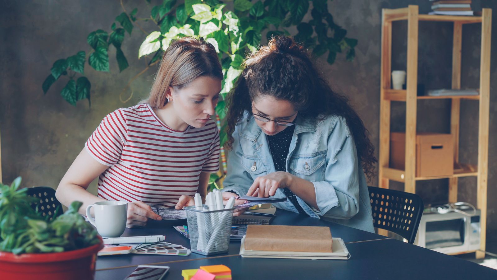 Two people working on a creative project at a desk with paper and pens