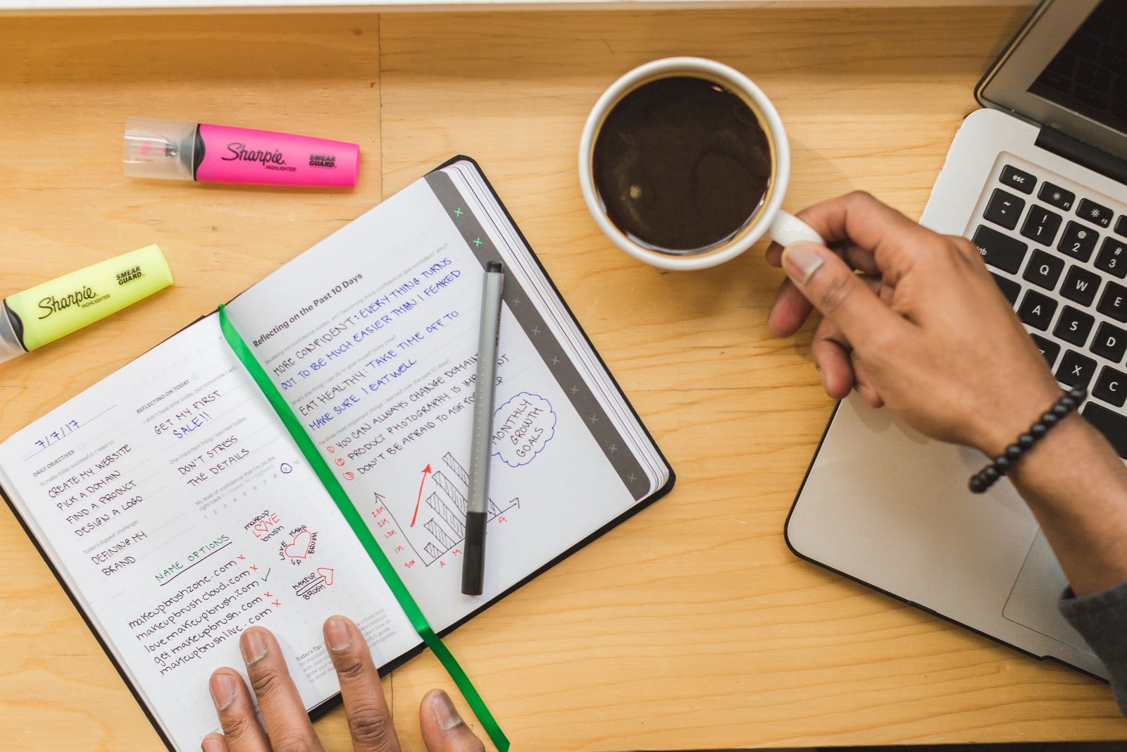 A notebook of handwritten review notes beside a laptop and a cup of coffee