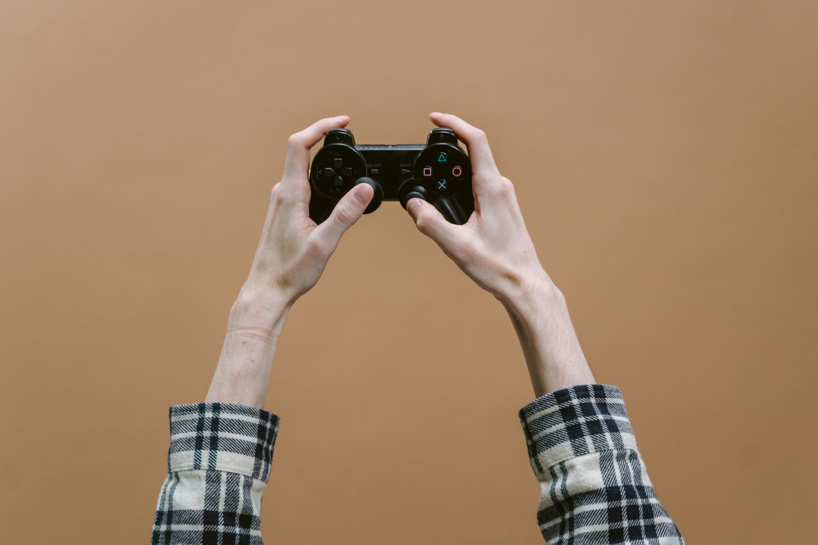 Two hands raising a gamepad against a plain brown wall