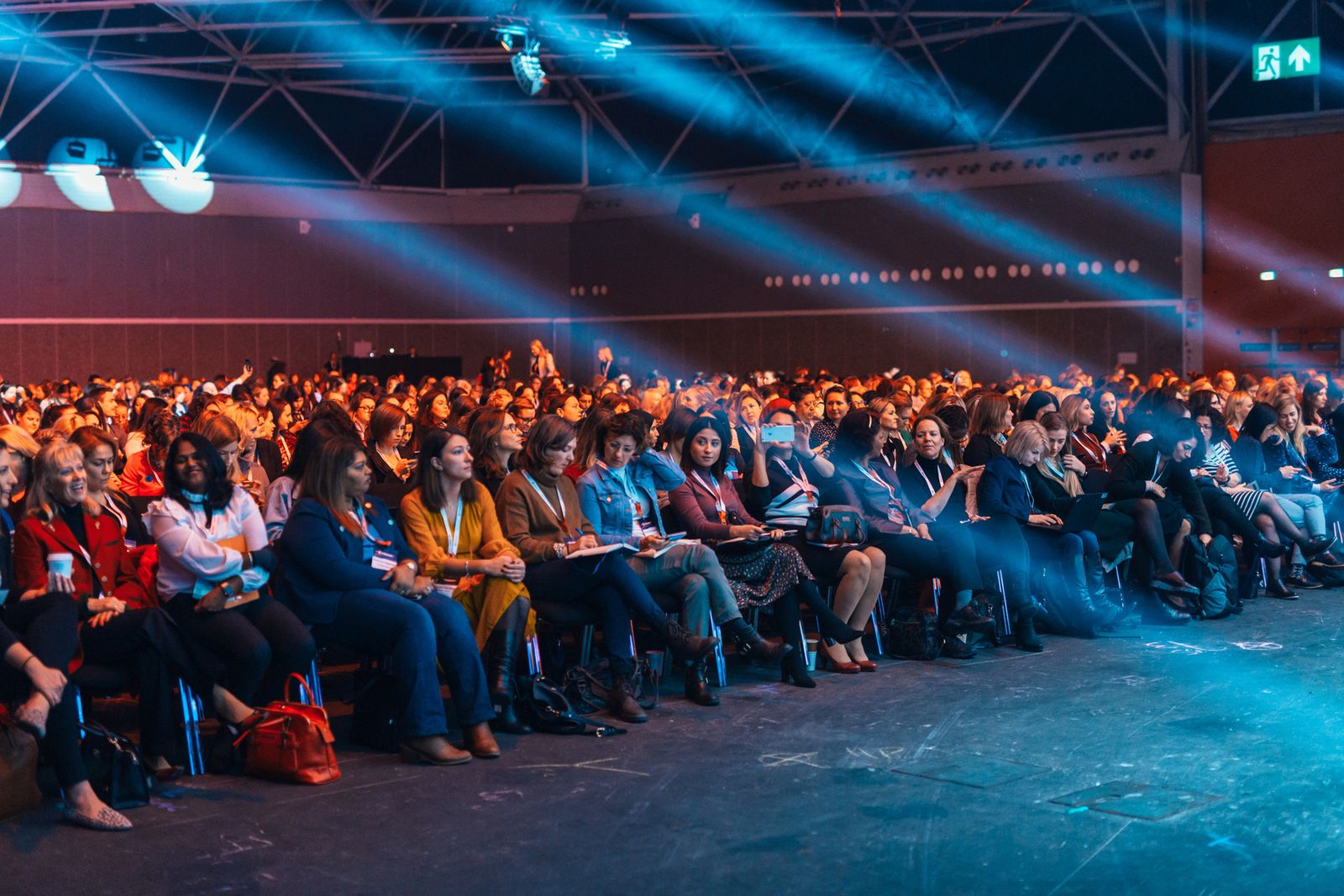 An audience in a darkened hall watching a stage presentation under blue lights