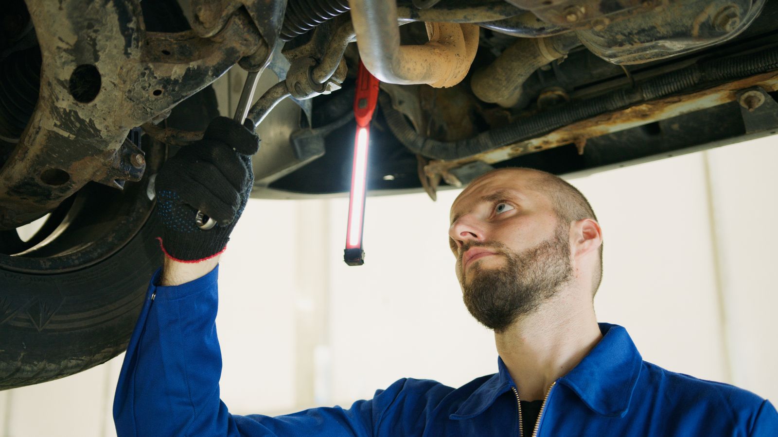 A mechanic checking the underside of a car with an inspection lamp