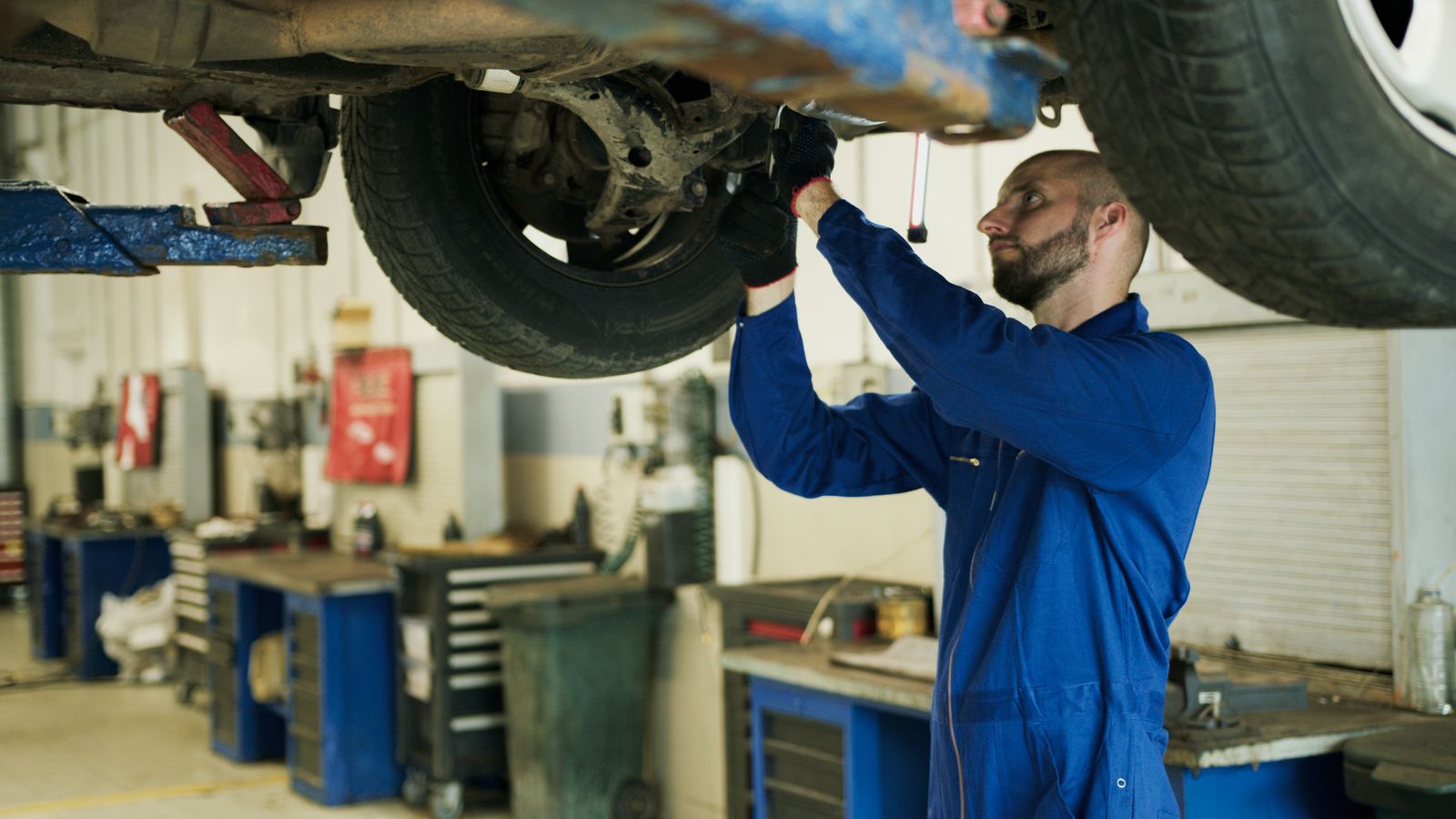 A mechanic in blue overalls inspecting the underside of a car on a lift