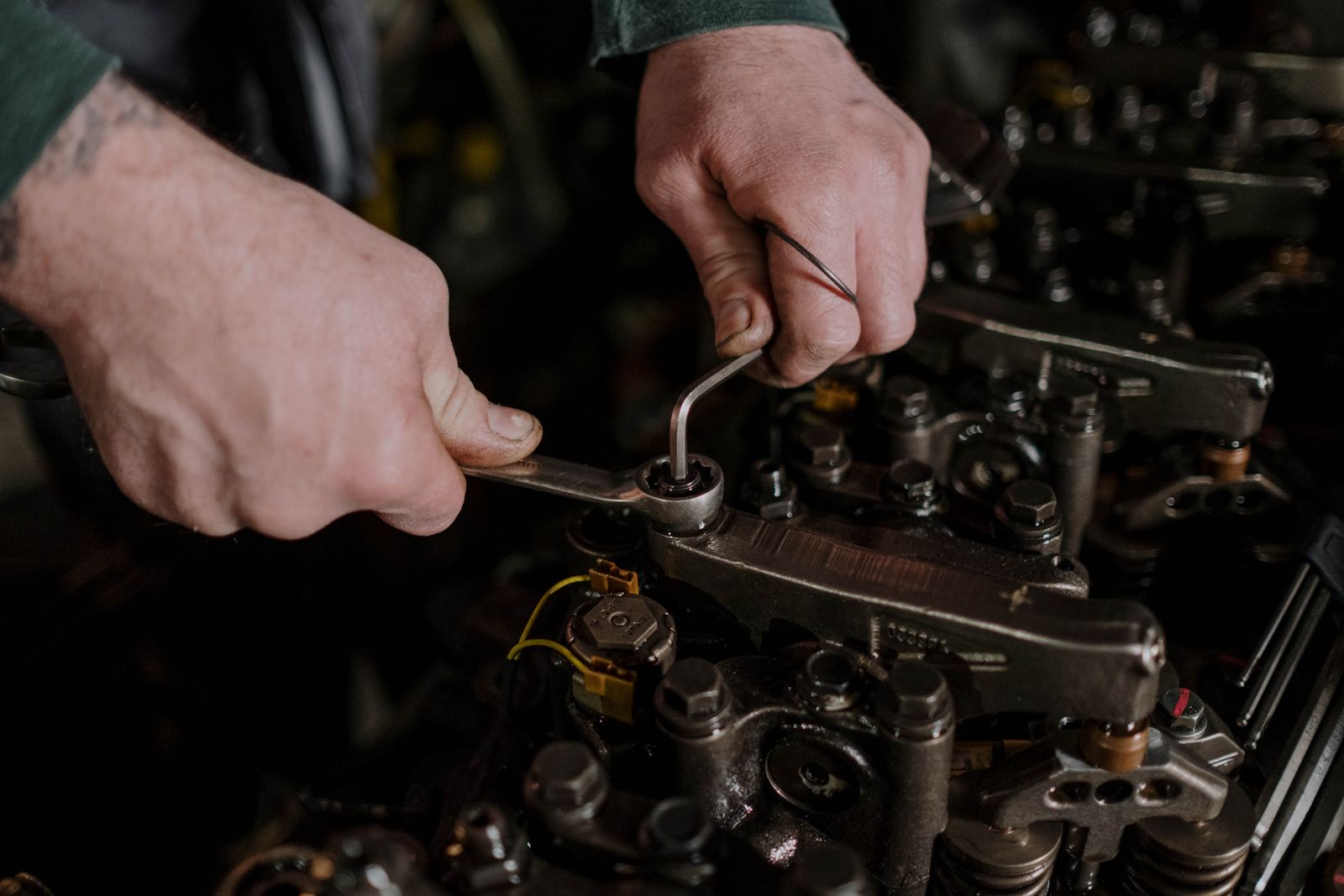 A mechanic's hands with a spanner and an Allen key working on an engine