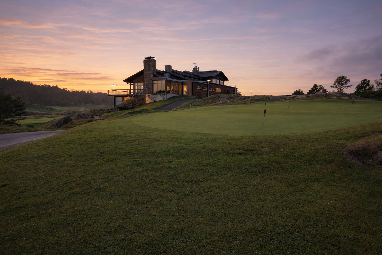 A clubhouse with lit windows above the course at sunset