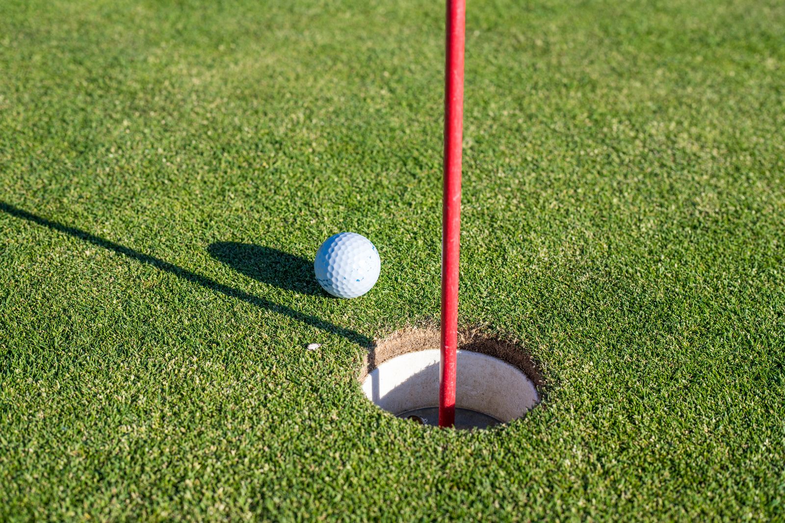 A golf ball resting at the edge of the hole beside a red flagstick