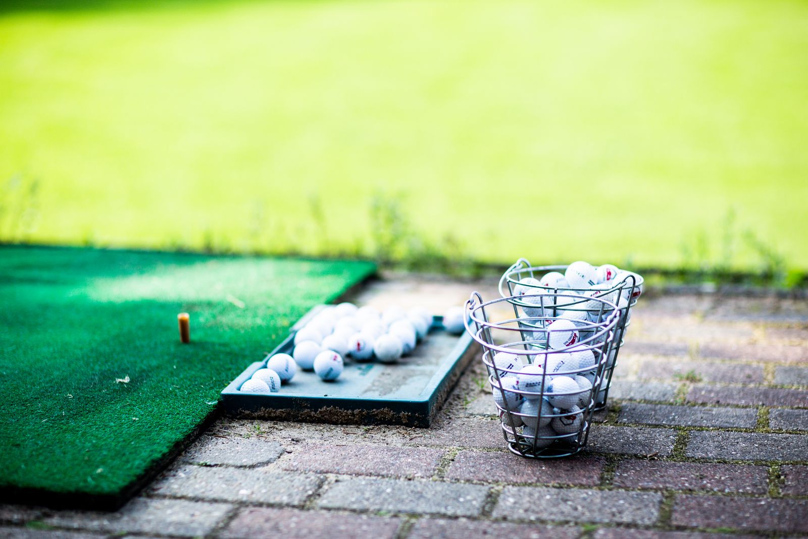 Practice balls in a wire basket and on a mat at an outdoor driving range