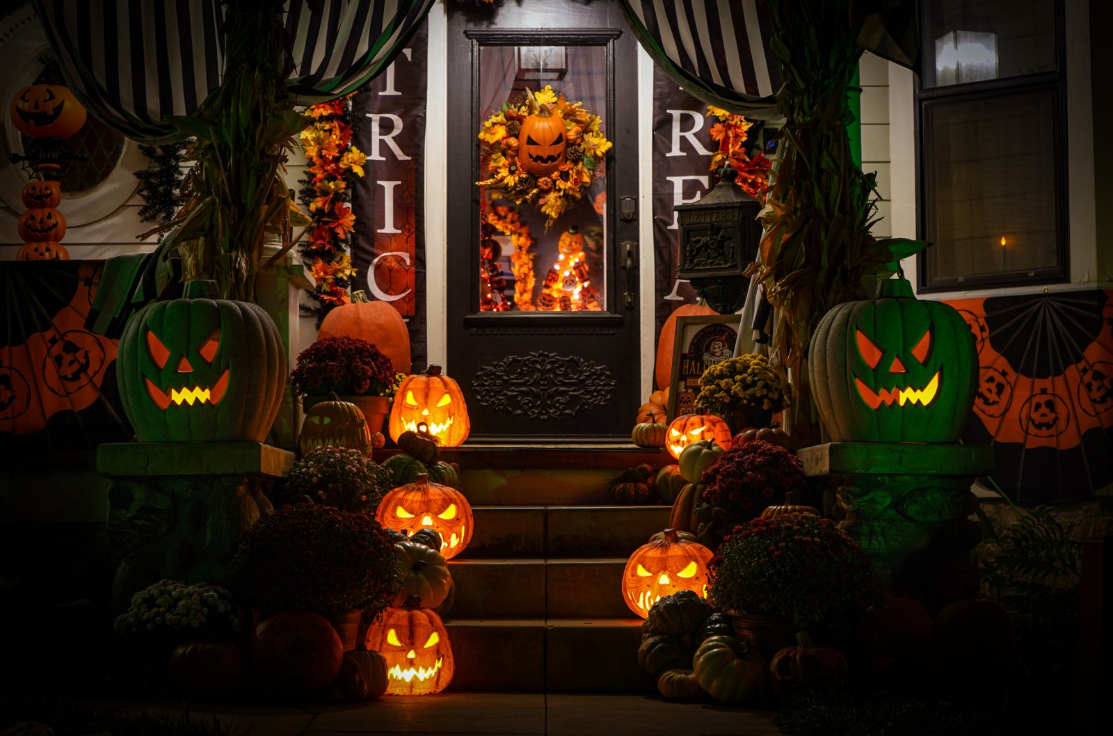 Jack-o'-lanterns glowing on the steps of a decorated porch at night