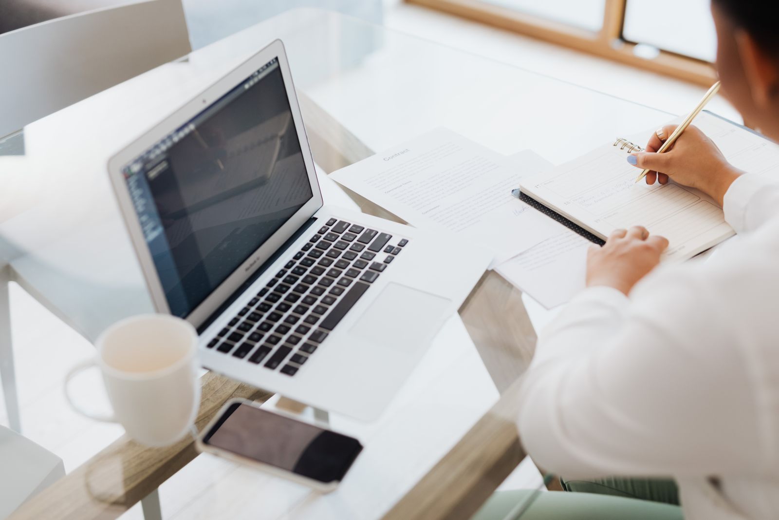 Person writing notes next to a laptop on a white desk