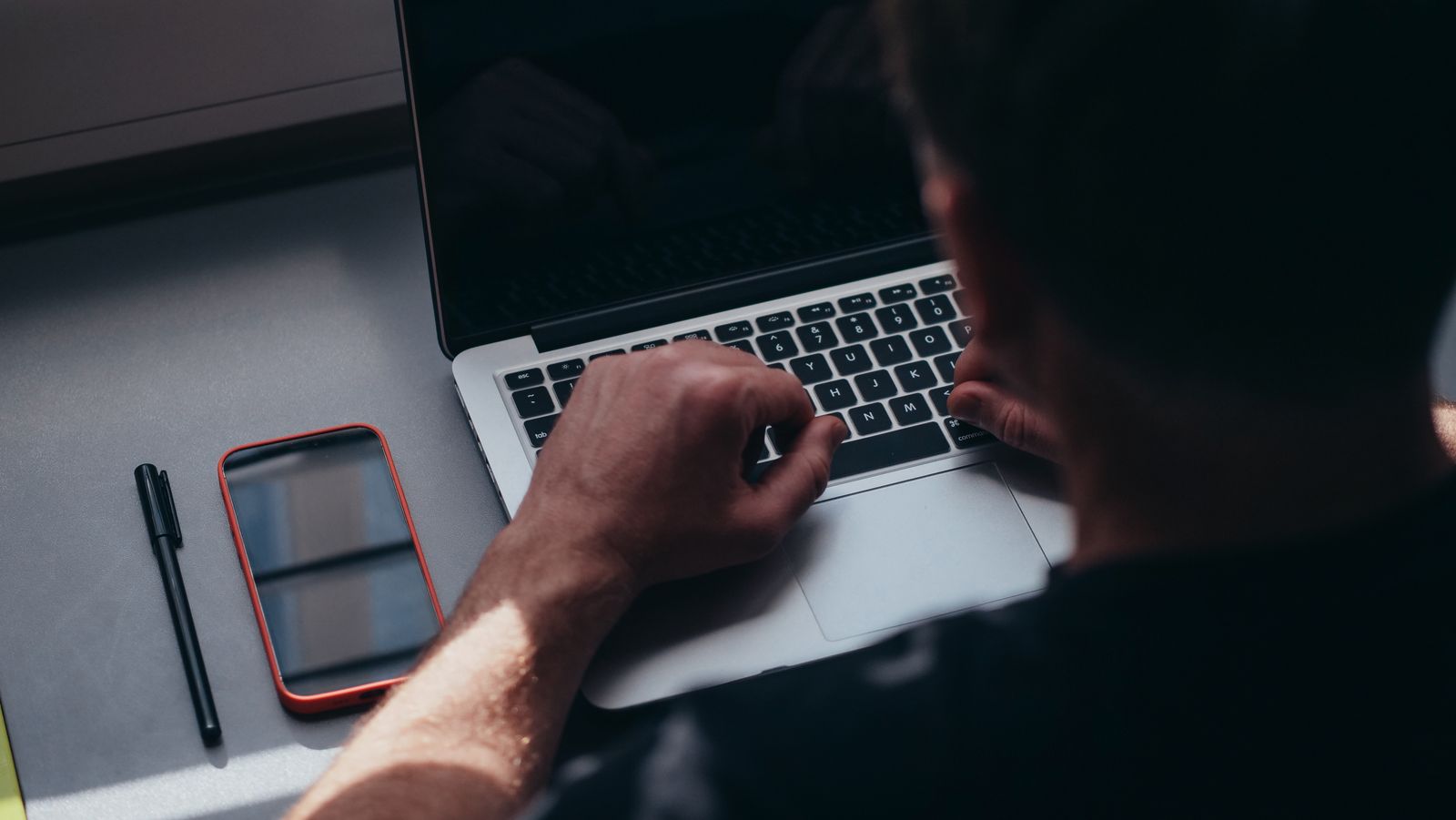 Person working on a laptop with a phone on the table