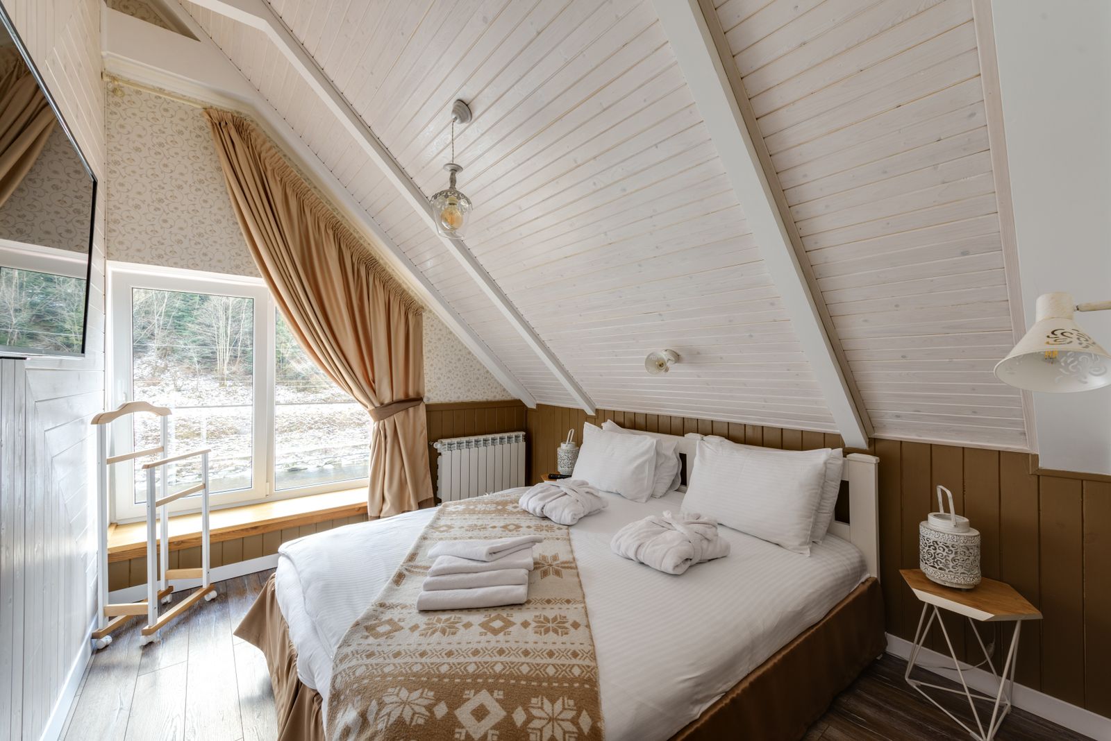 An attic bedroom with a sloped white ceiling, a skylight window and a made double bed
