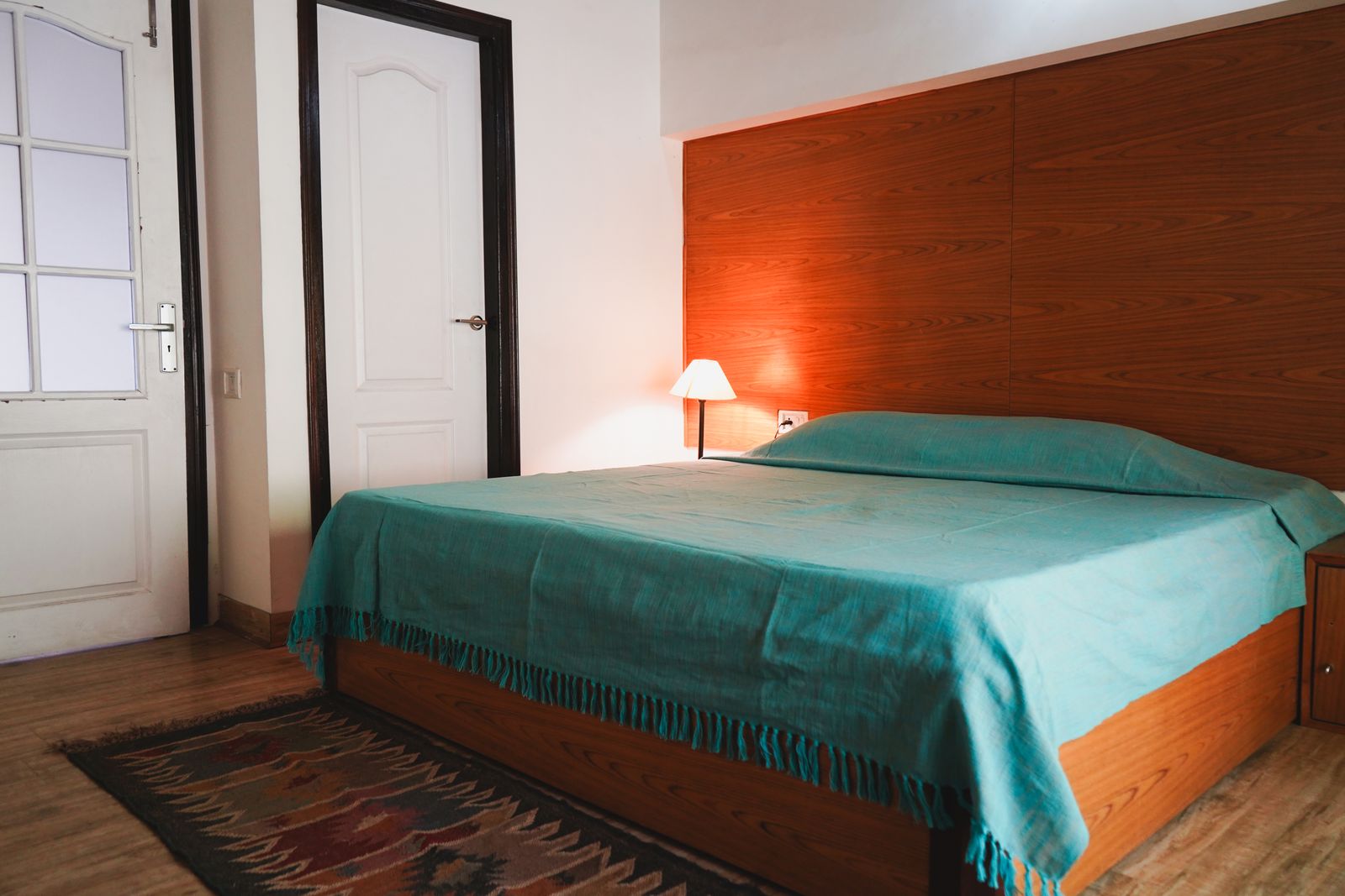 A Classic double room with a teal bedspread, wooden headboard and a rug on the floor