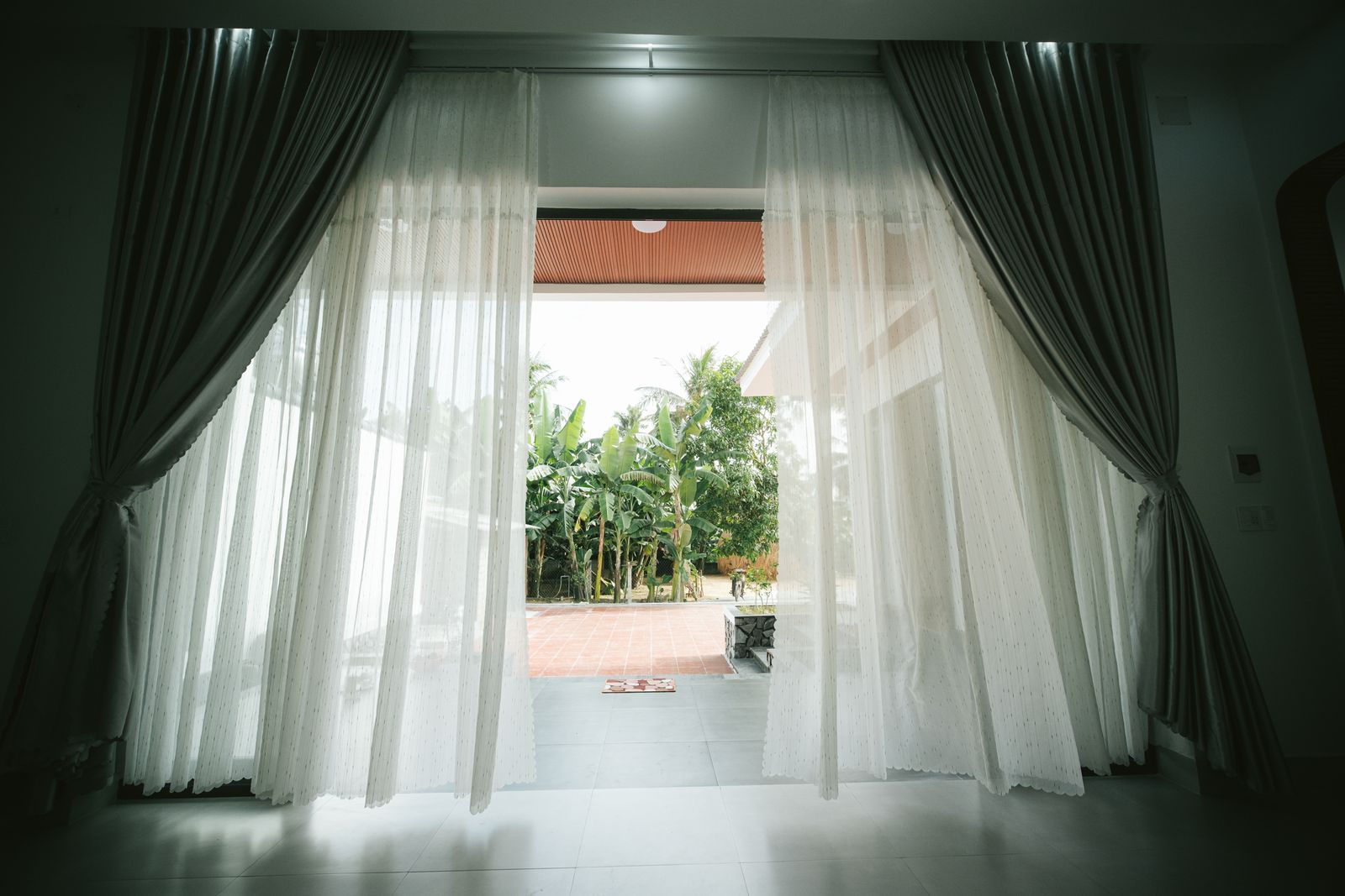 Open terrace doors with white curtains and a green garden outside