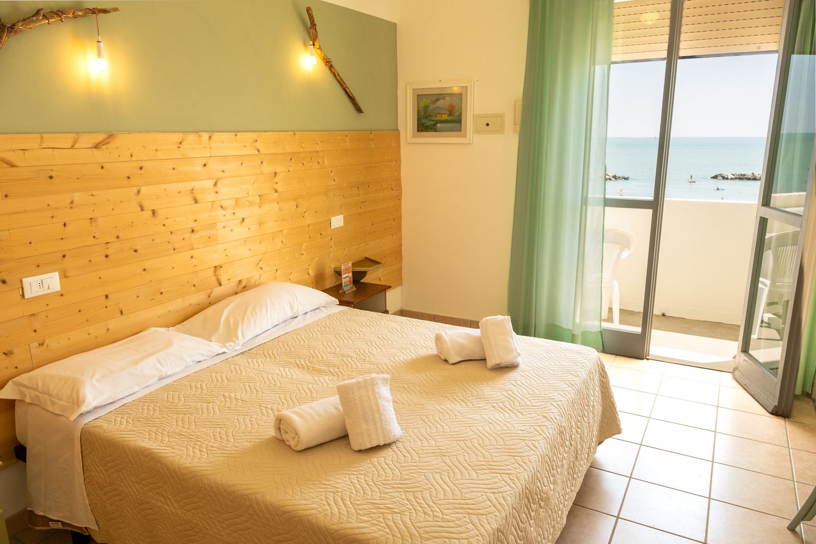 A bright room with a double bed and a glass door open onto a balcony over the sea