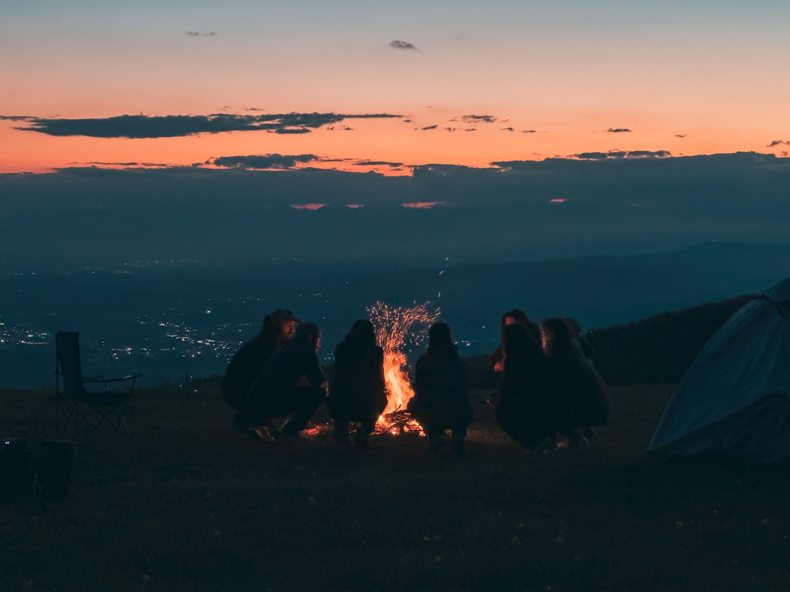 A group sitting around a campfire on a hillside at dusk