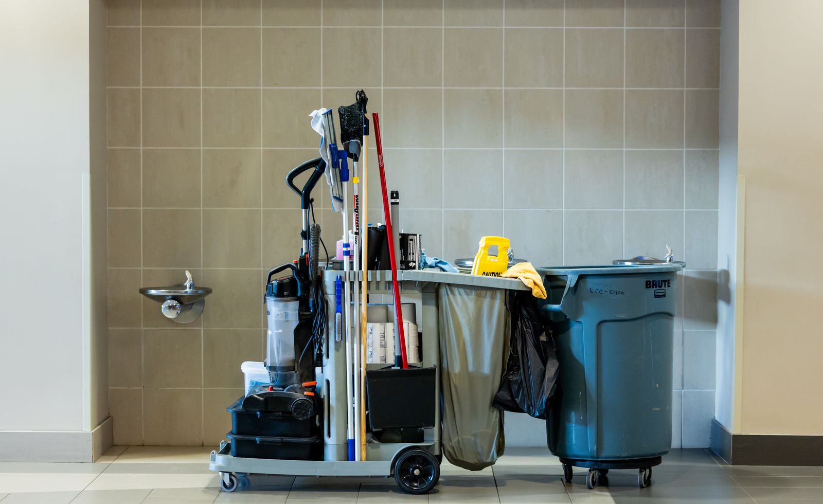 A cleaning trolley with mops, cloths and bins in a tiled corridor