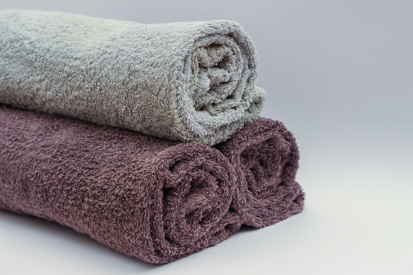 Rolled bath towels in grey and plum stacked together