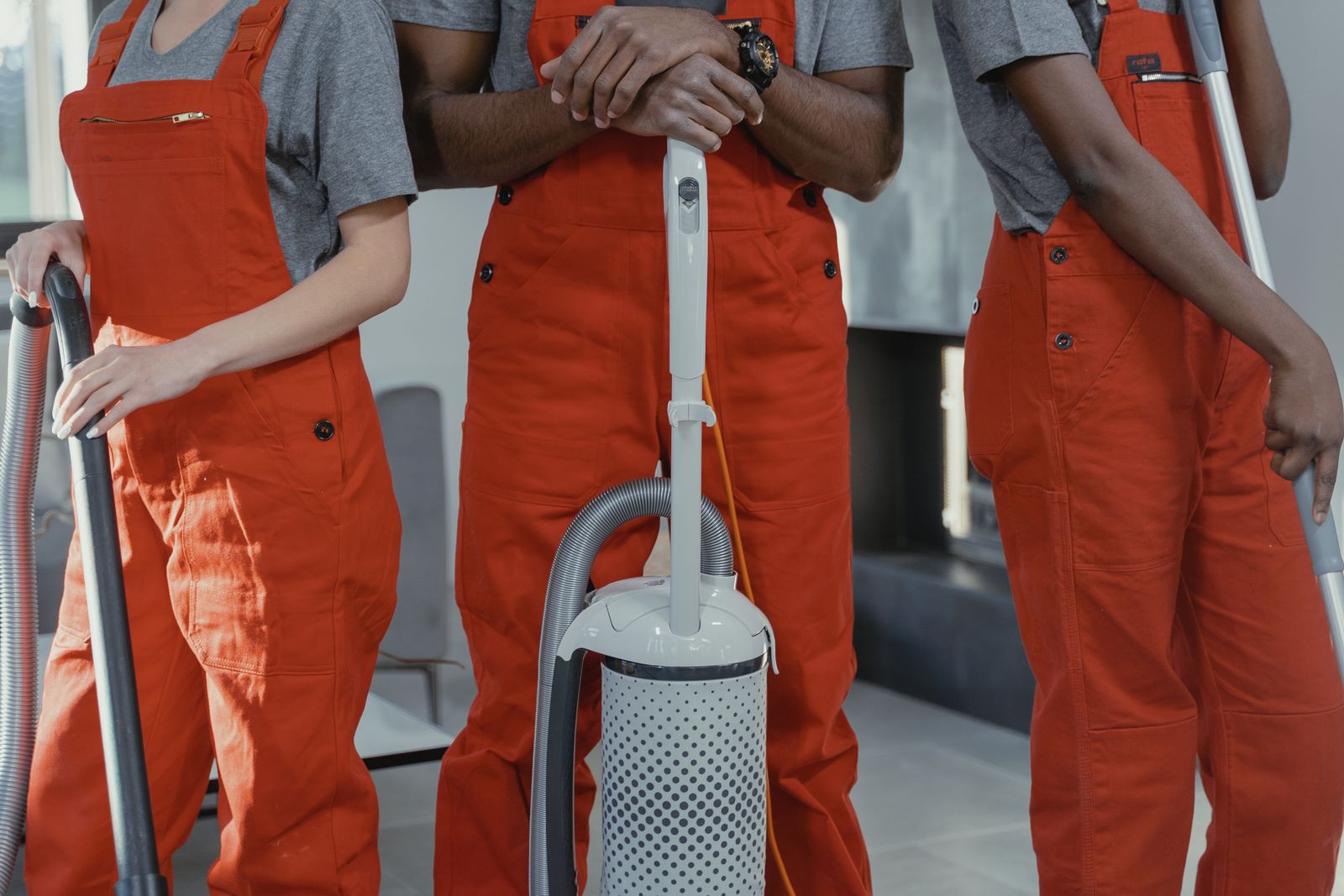 Three cleaners in red overalls holding a vacuum cleaner and cleaning tools