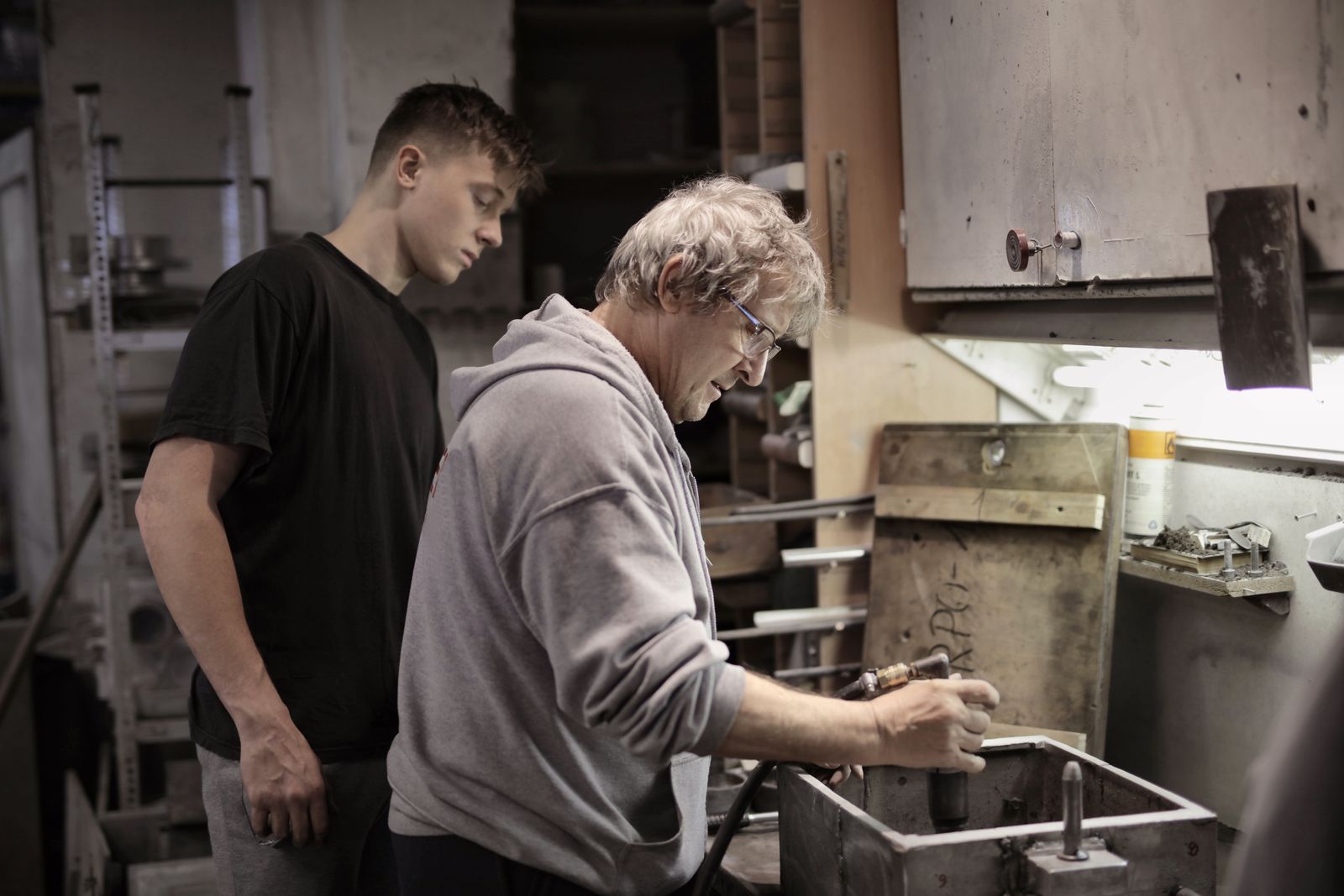 An experienced machinist showing a trainee a part at the workbench