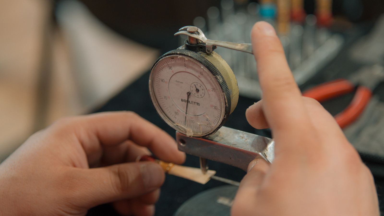 Hands checking a machined part with a dial indicator