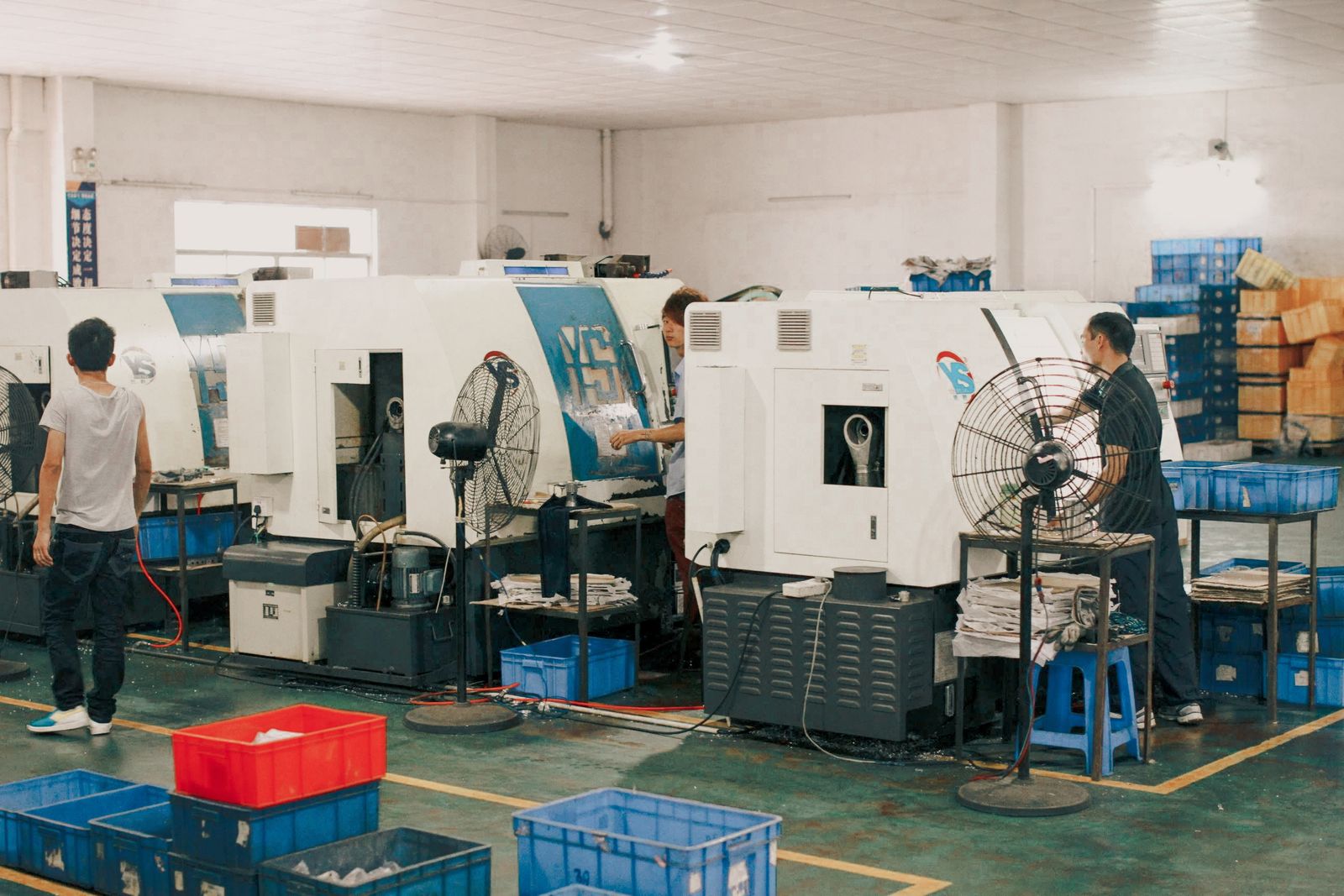 Row of CNC machines on a shop floor with operators and parts crates