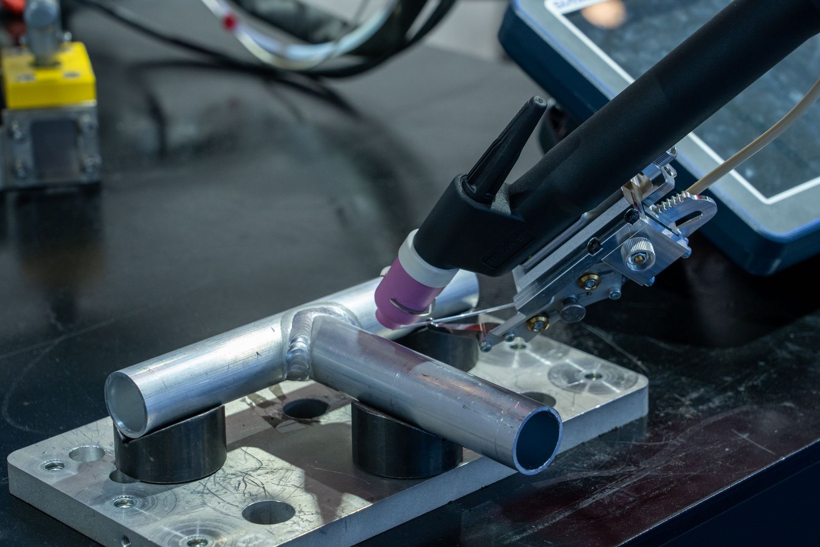 TIG torch welding an aluminium tube held in a jig on the bench