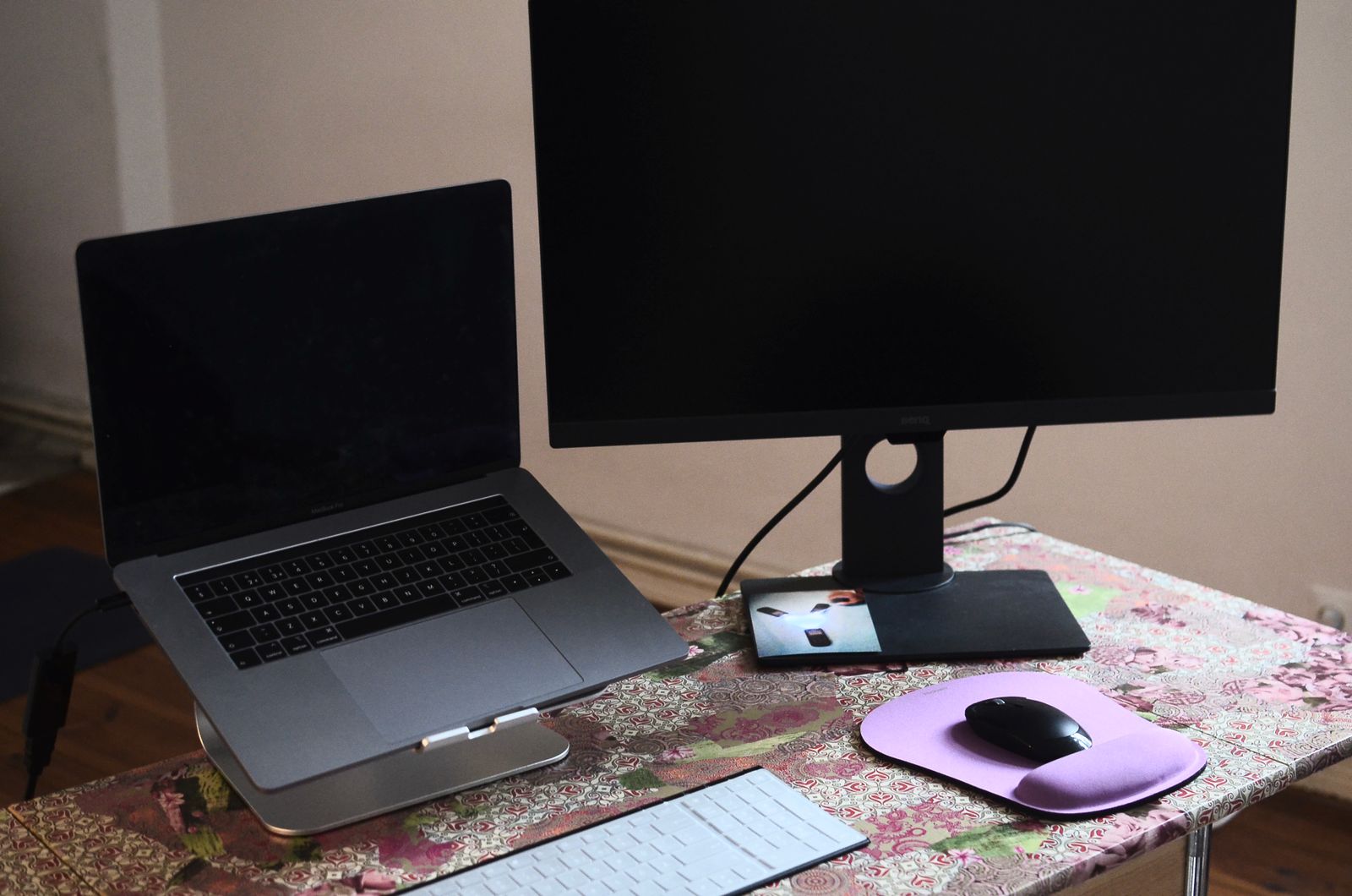 A laptop on a stand next to a monitor, keyboard and mouse on a desk