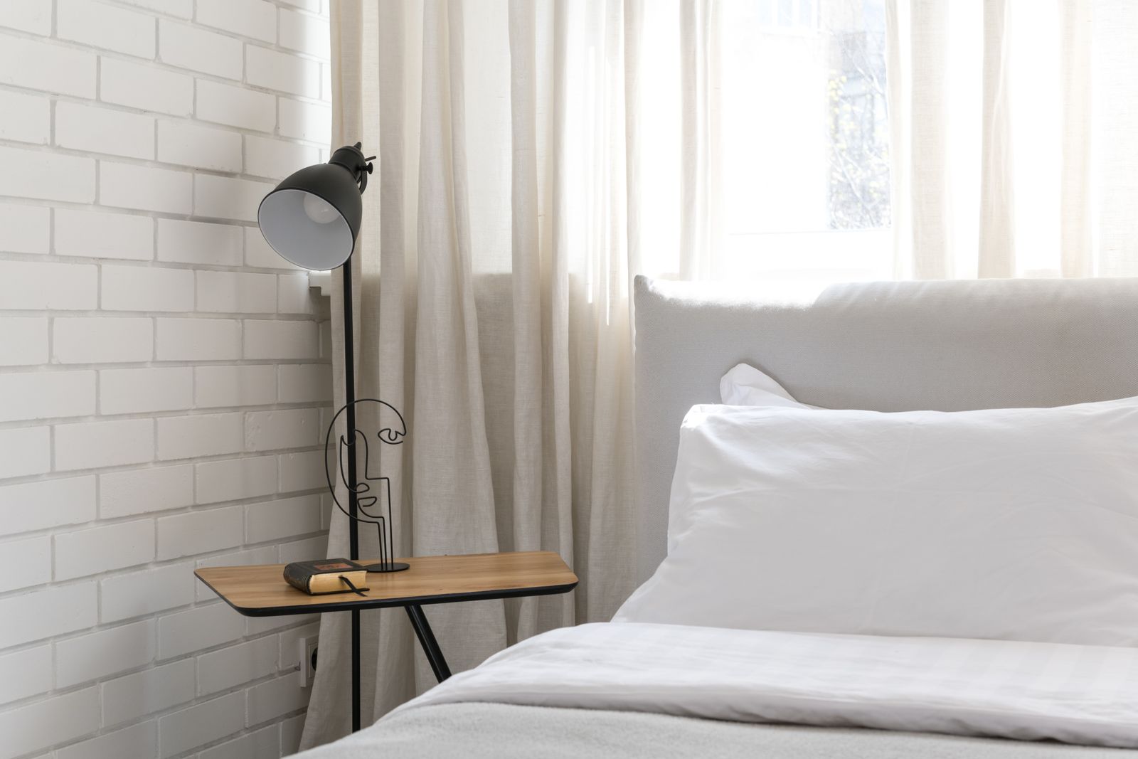Bedroom with a white bed, a wall lamp and a small side table by the window