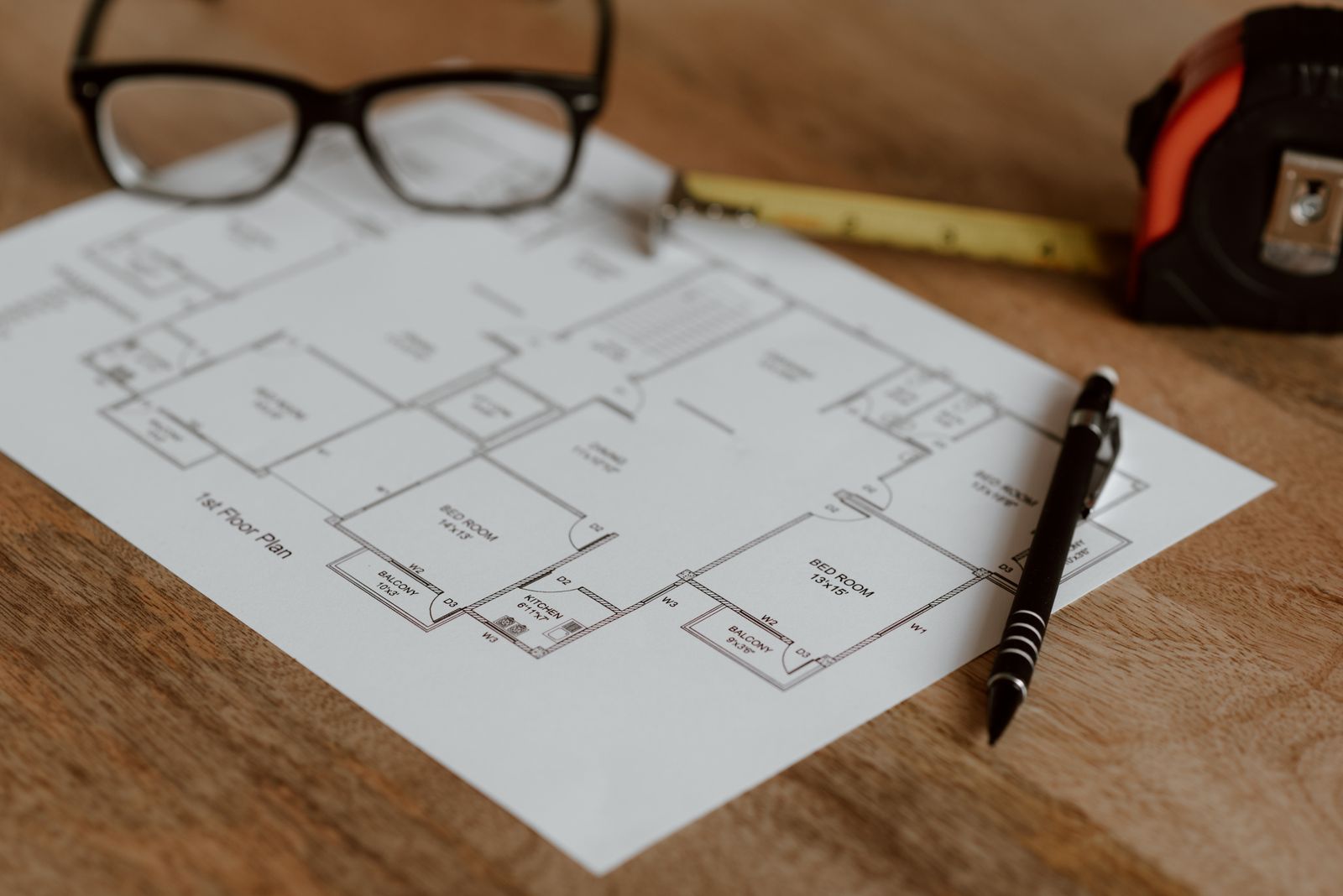 A printed floor plan on a desk with a pen, a ruler and reading glasses
