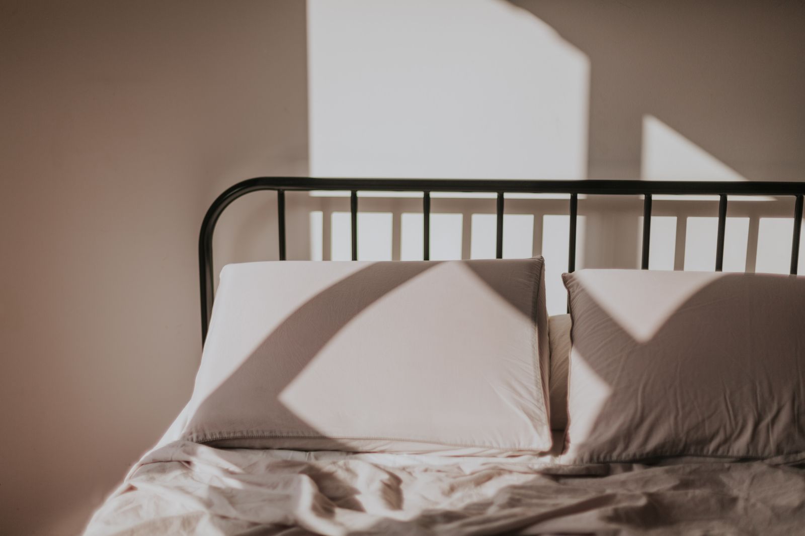 Morning sun casting window shadows across a bed with linen pillows