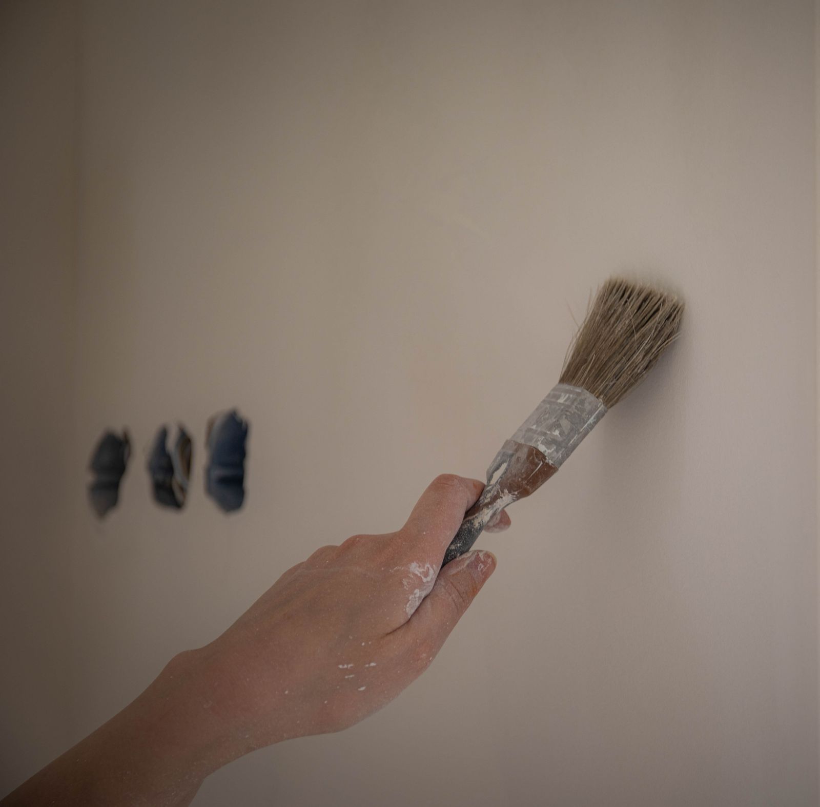 A hand painting a white wall beside three test patches of colour