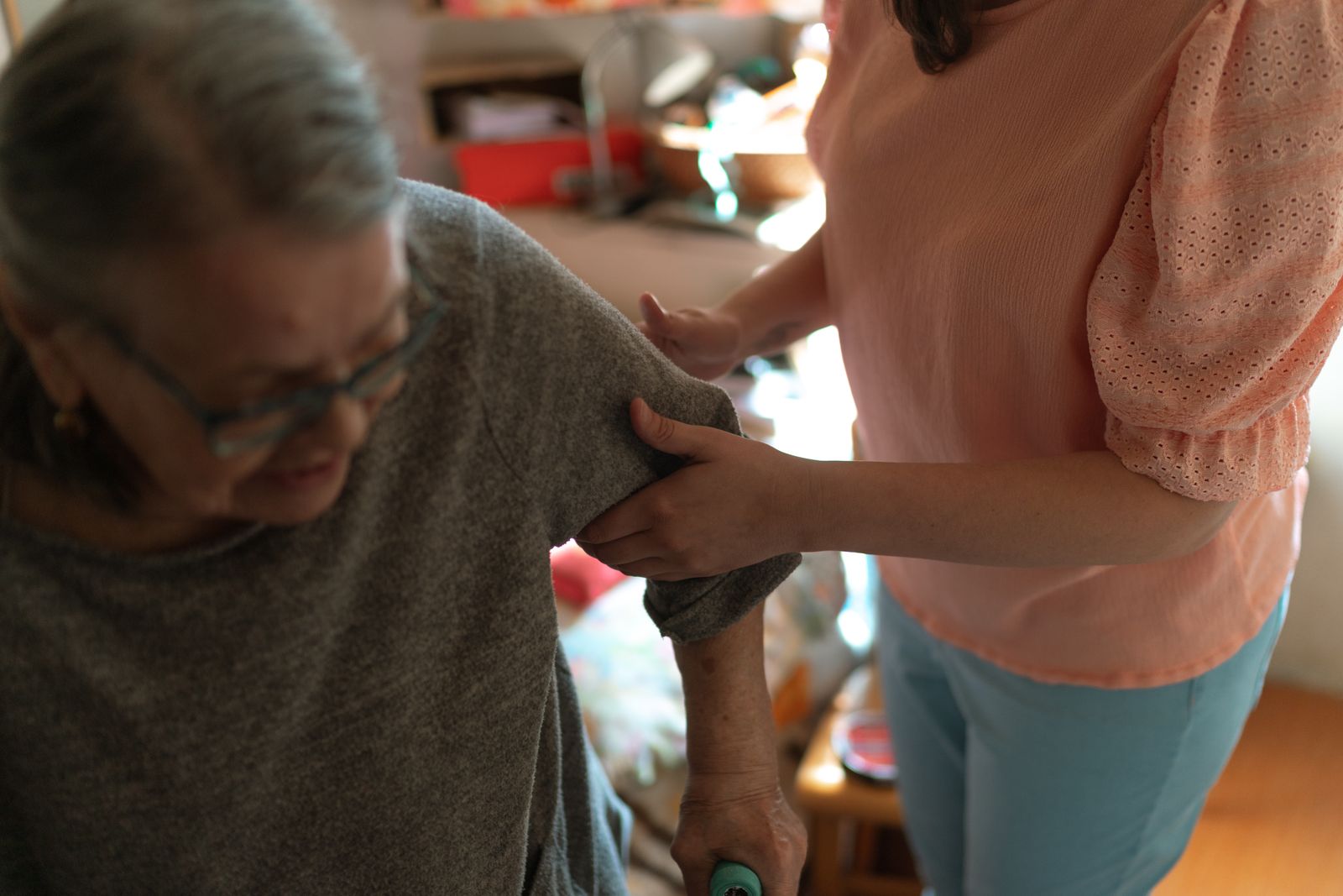 A carer steadying an older woman by the arm as she stands up at home