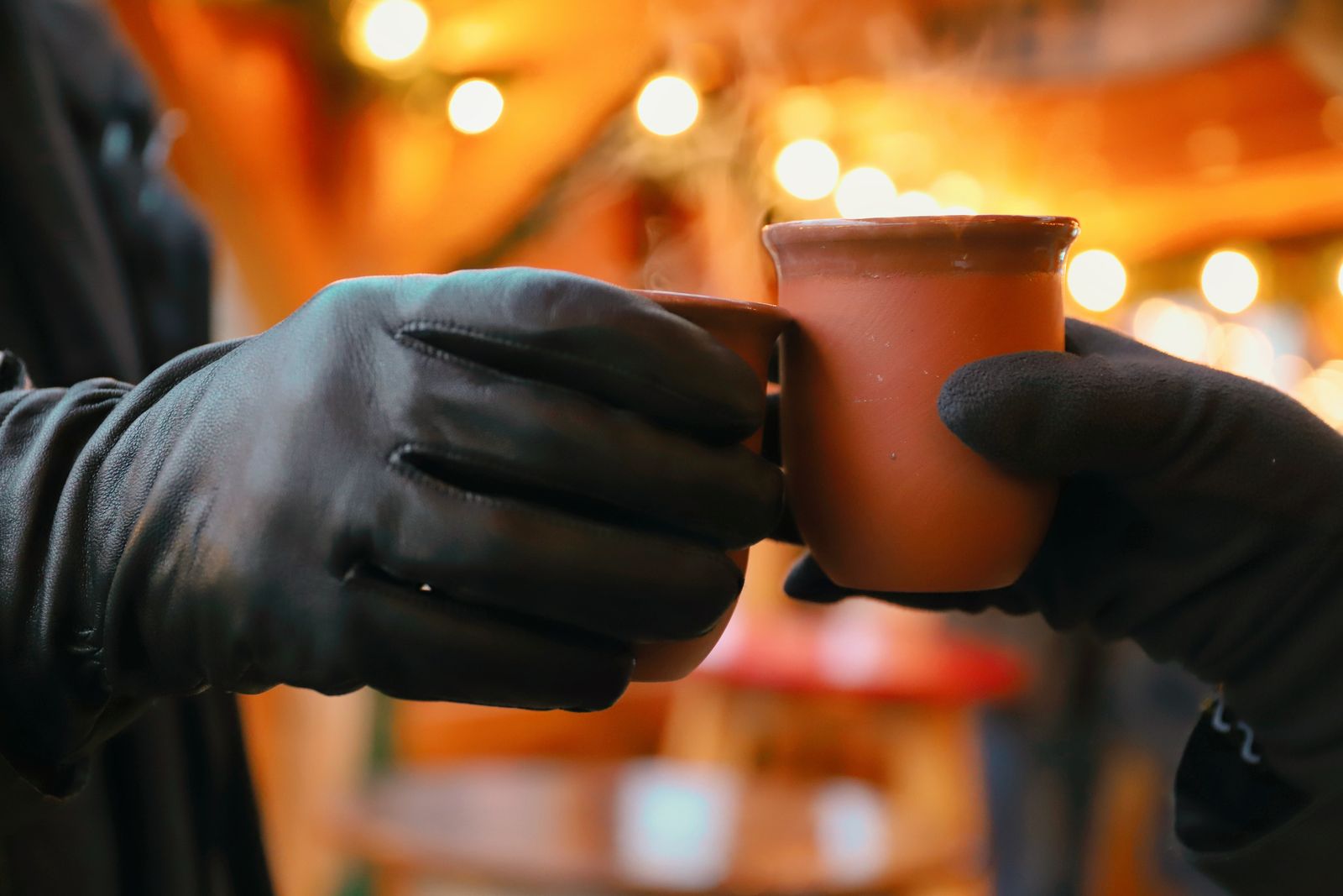 Two gloved hands clinking mugs of mulled wine at a market stall