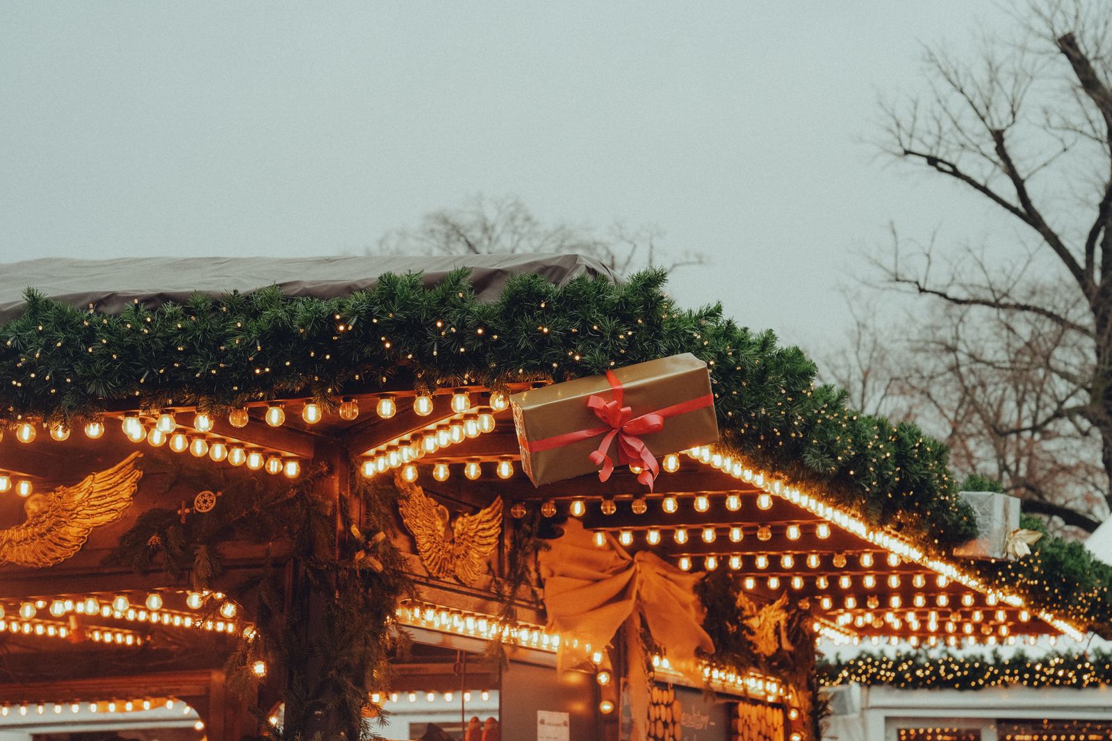 Roof of a wooden market hut lined with warm string lights and fir garlands at dusk