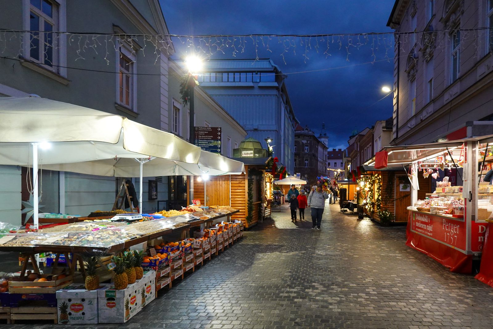 A street of lit market stalls on cobblestones at twilight