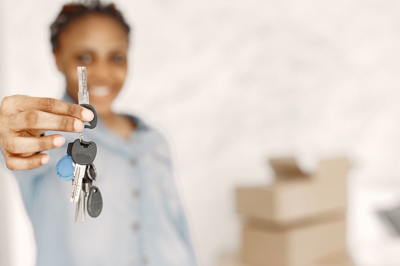 A hand holding a set of house keys in front of moving boxes
