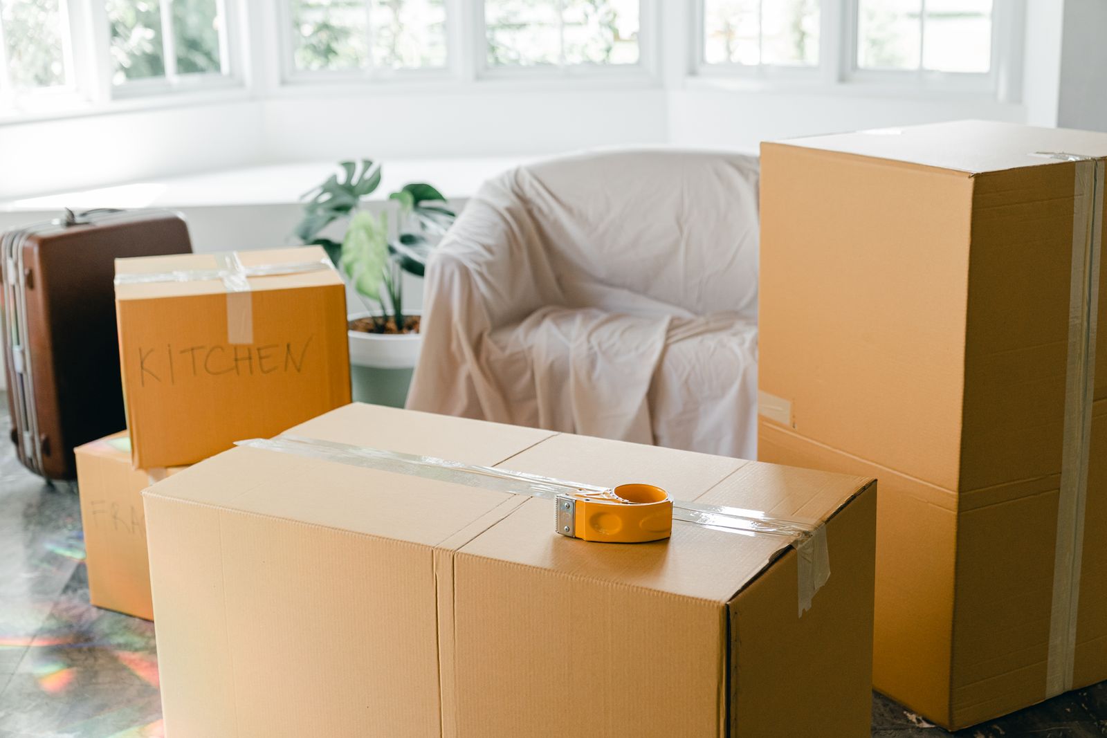 Packed cardboard boxes and a suitcase on the floor of a bright room