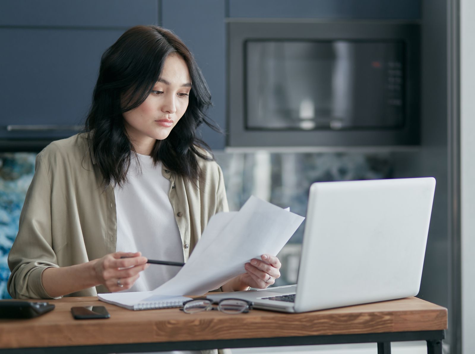 A woman sorting printed documents beside her laptop at home