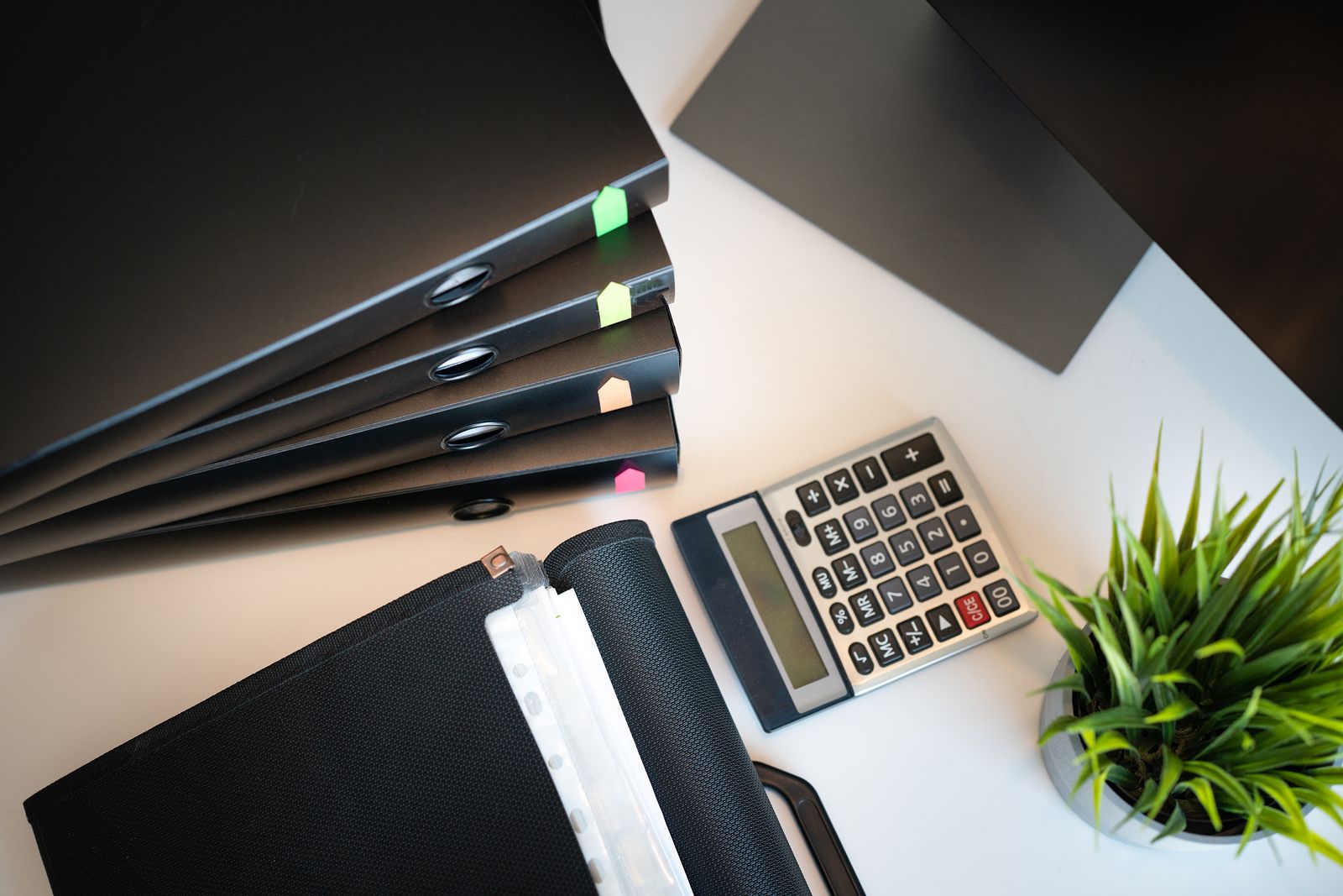 A calculator, reading glasses and black folders on a white desk