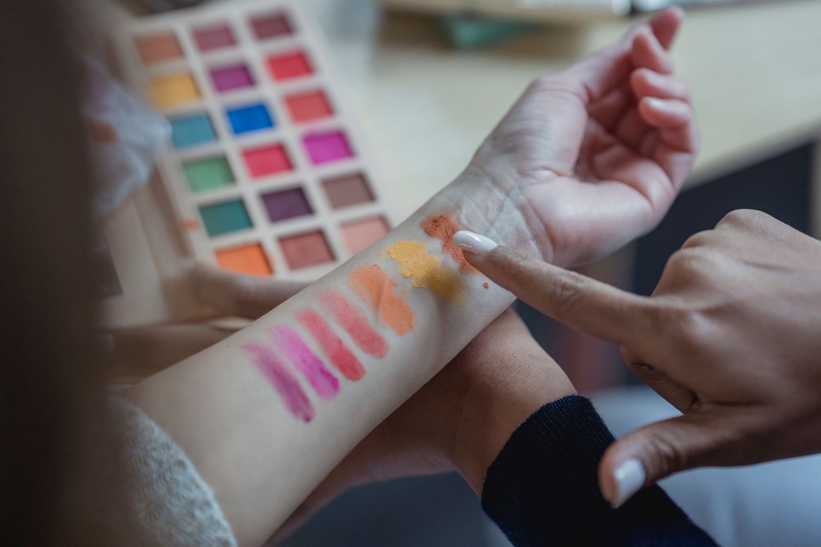 An artist points at eyeshadow swatches painted on a client's wrist