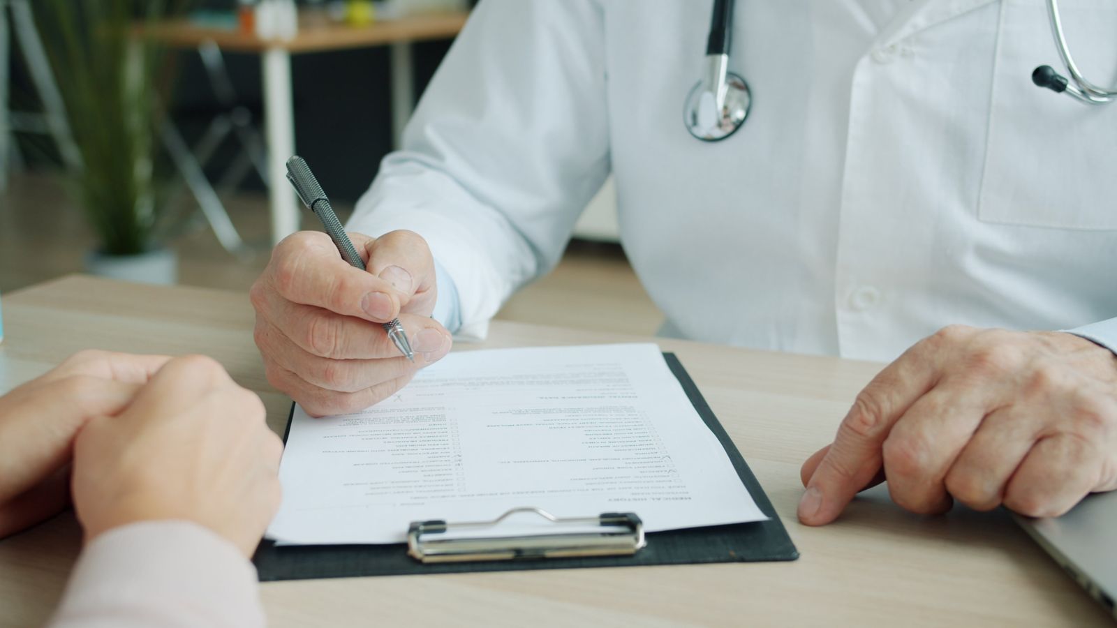 A doctor and a patient going through a form at a desk, only their hands in view