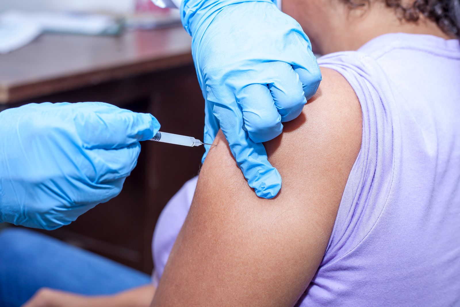 A nurse in blue gloves giving a vaccine in an upper arm