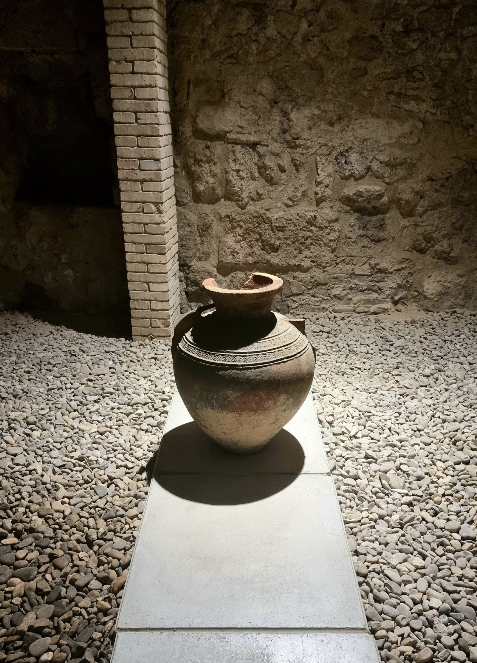 Ancient storage jar on a bed of gravel, lit from above