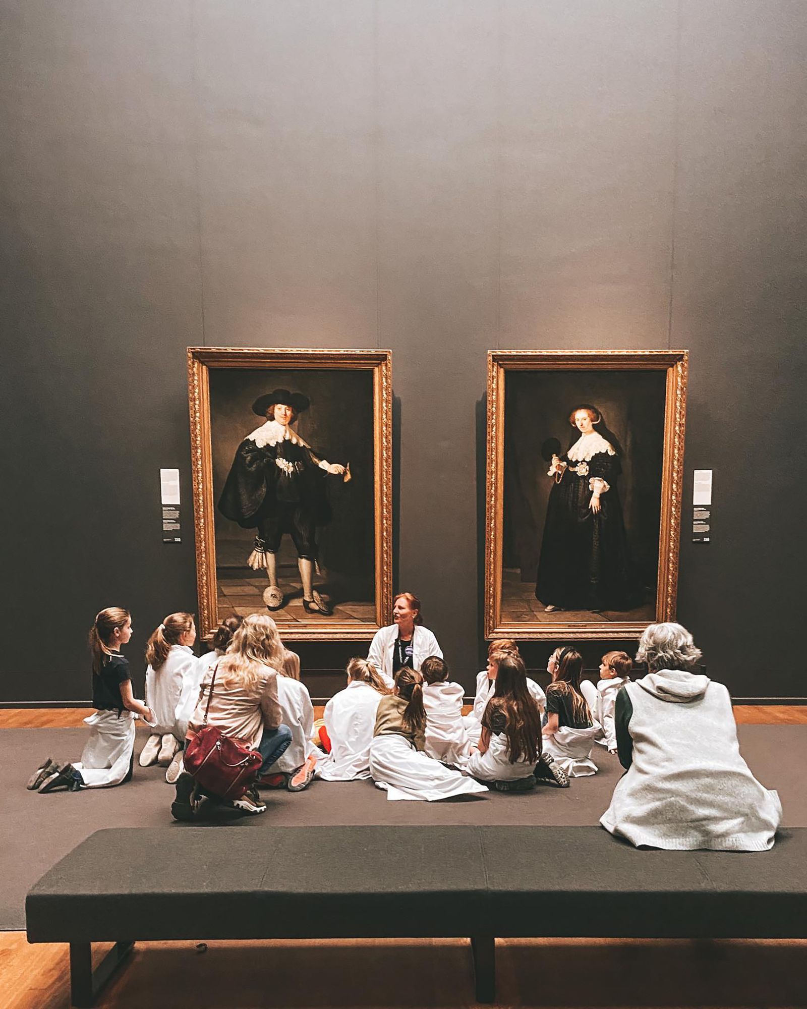 A school group sitting on the floor in front of two portraits