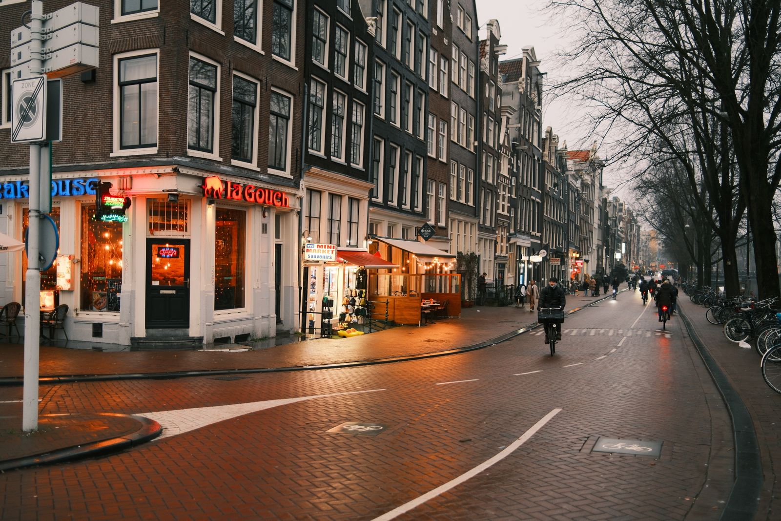 Cyclists on a town street at dusk, shop windows lit