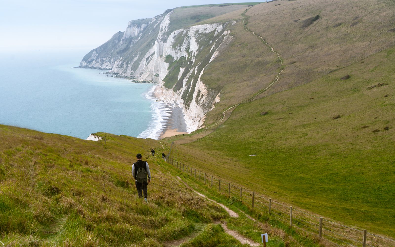A walker on a grassy cliff path high above the sea