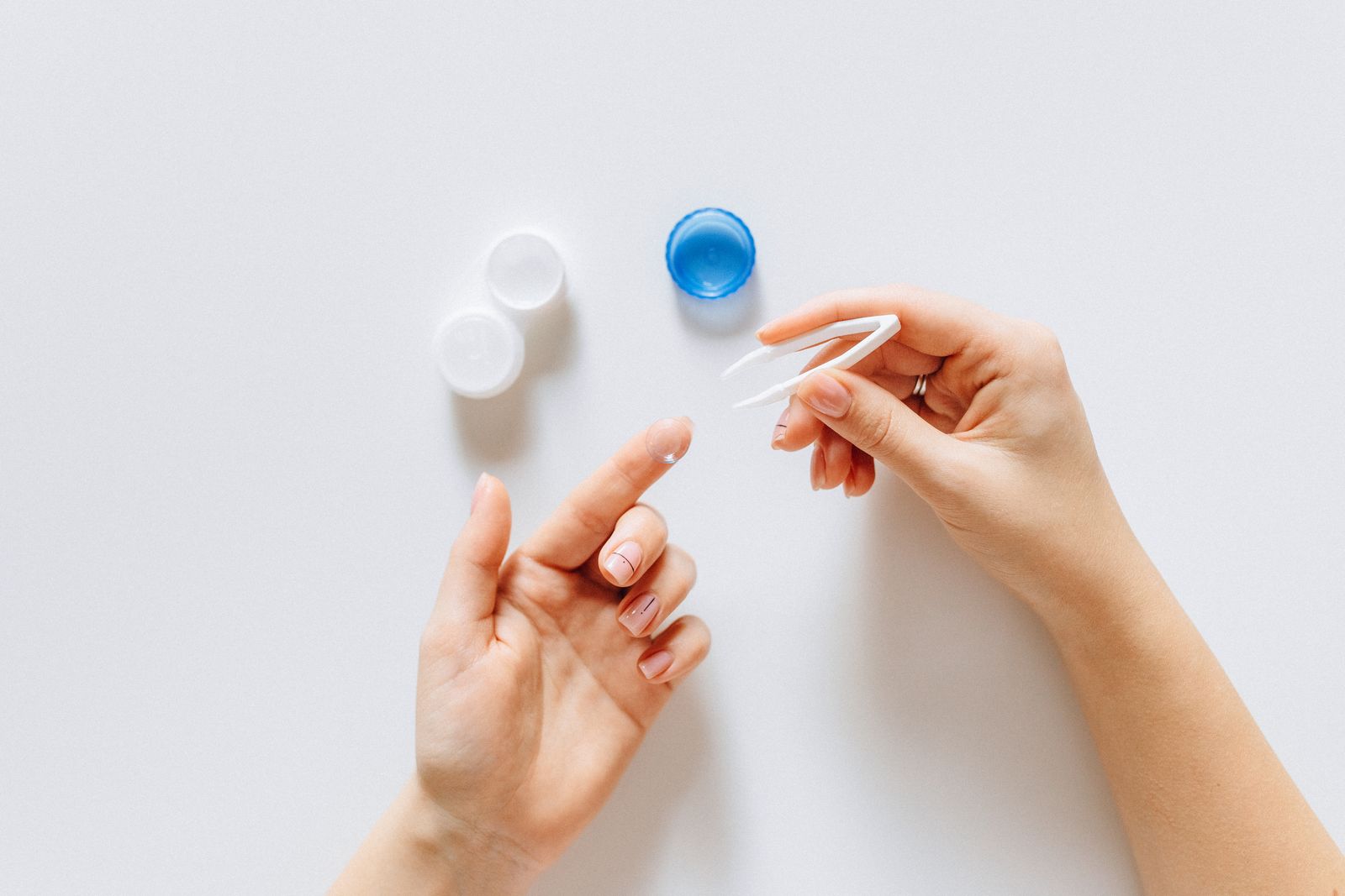 Fingers holding a contact lens over its case on a white table