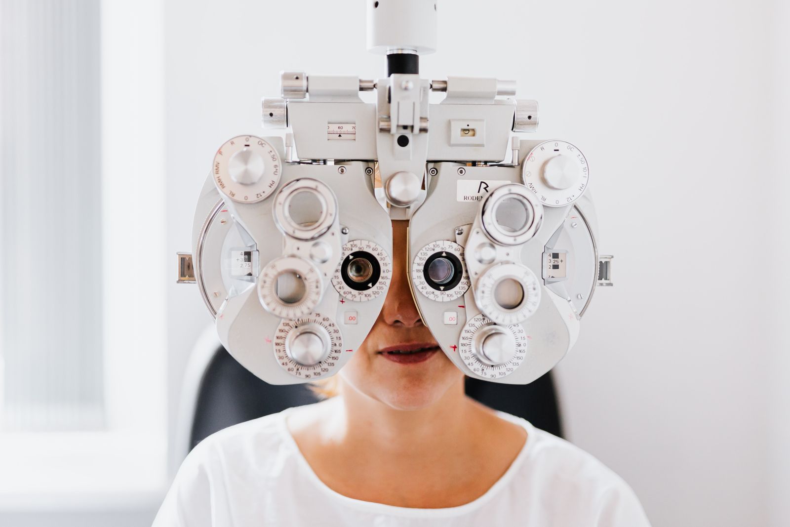 A person behind a phoropter during an eye test, face hidden by the instrument